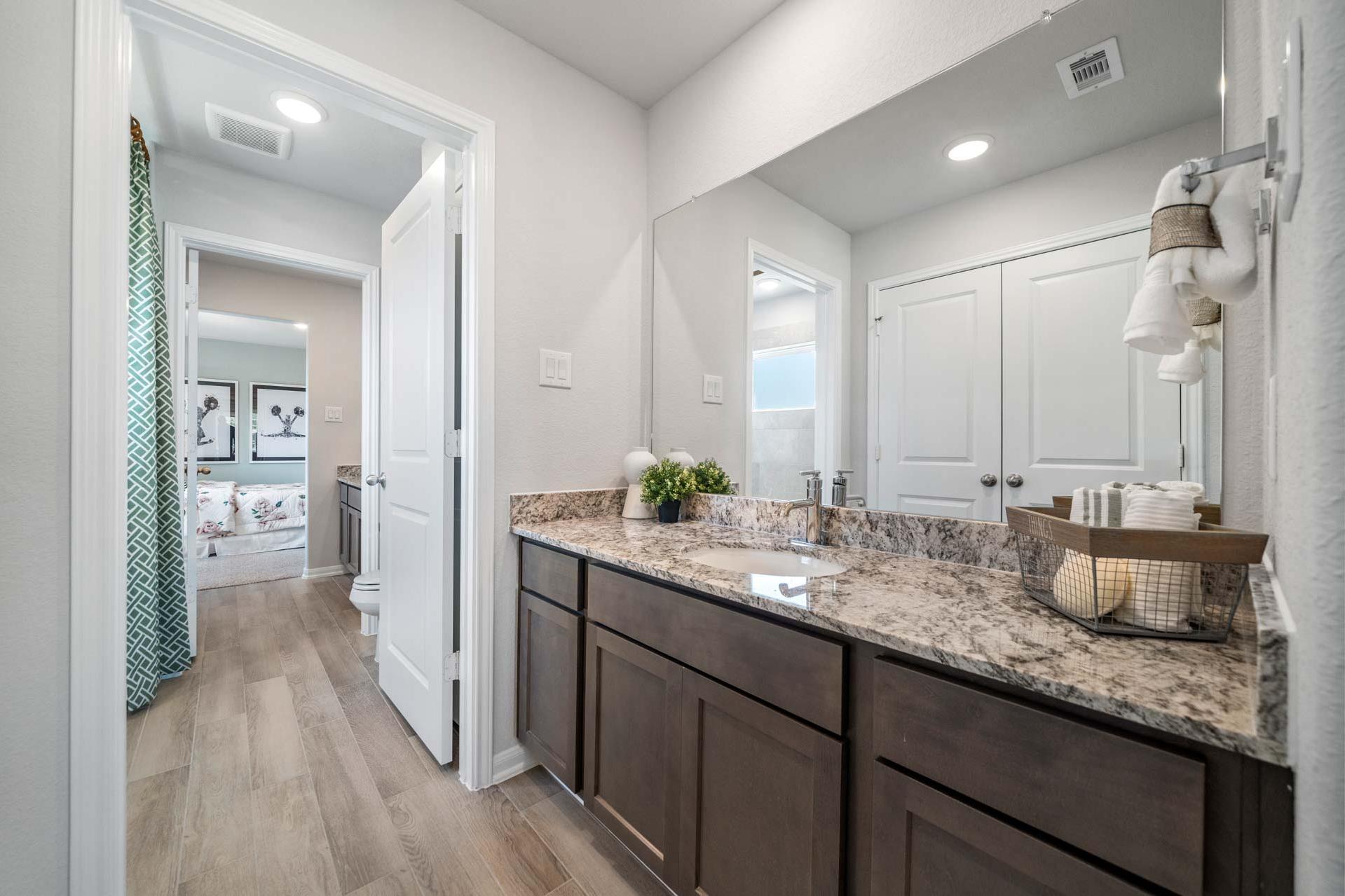 Spacious primary bathroom at Windmill Estates in Magnolia Texas featuring double vanity with granite counters and hardwood floors