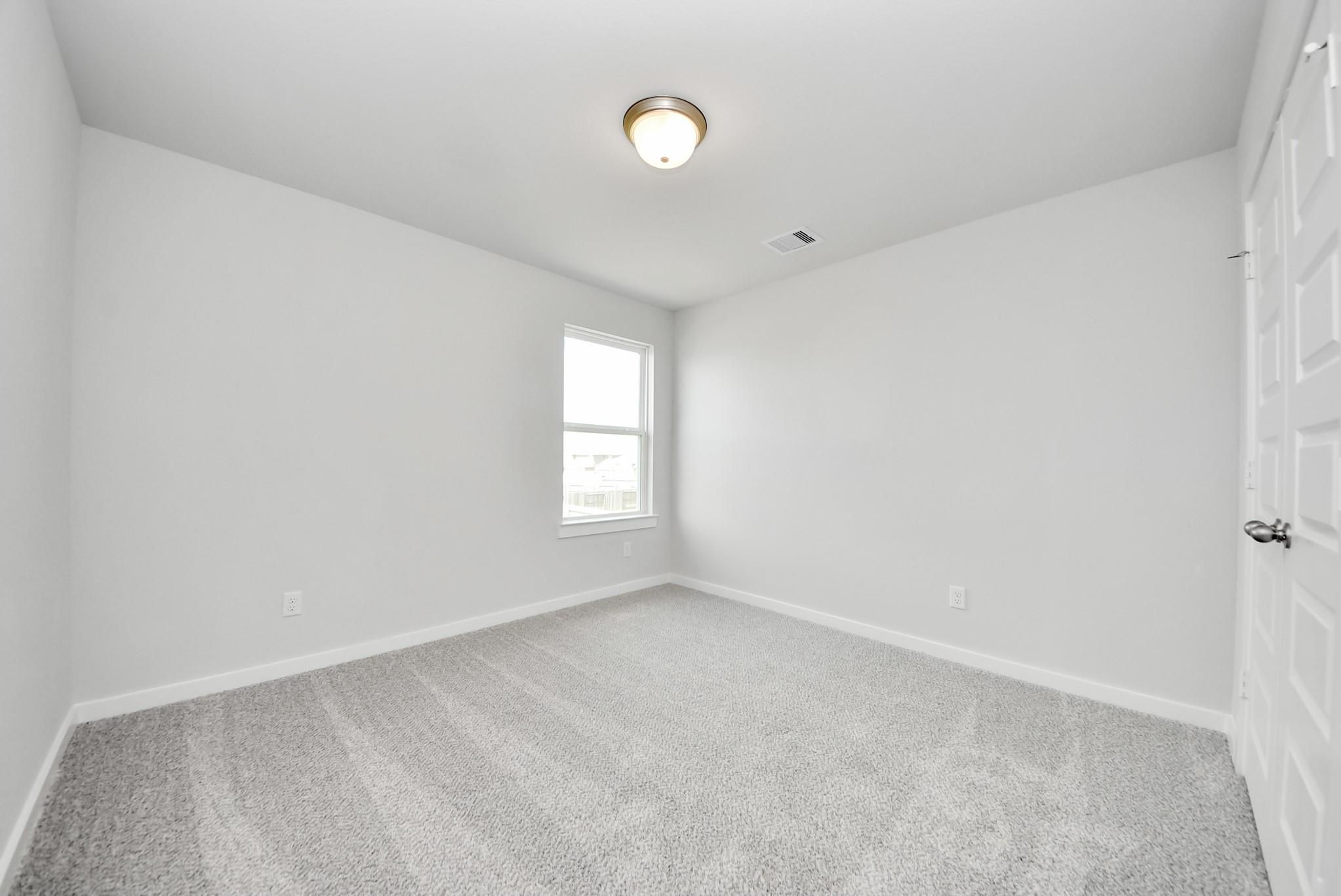Bright, carpeted secondary bedroom with a window in The Verano B floor plan by Davidson Homes in Sunterra, Katy, Texas.