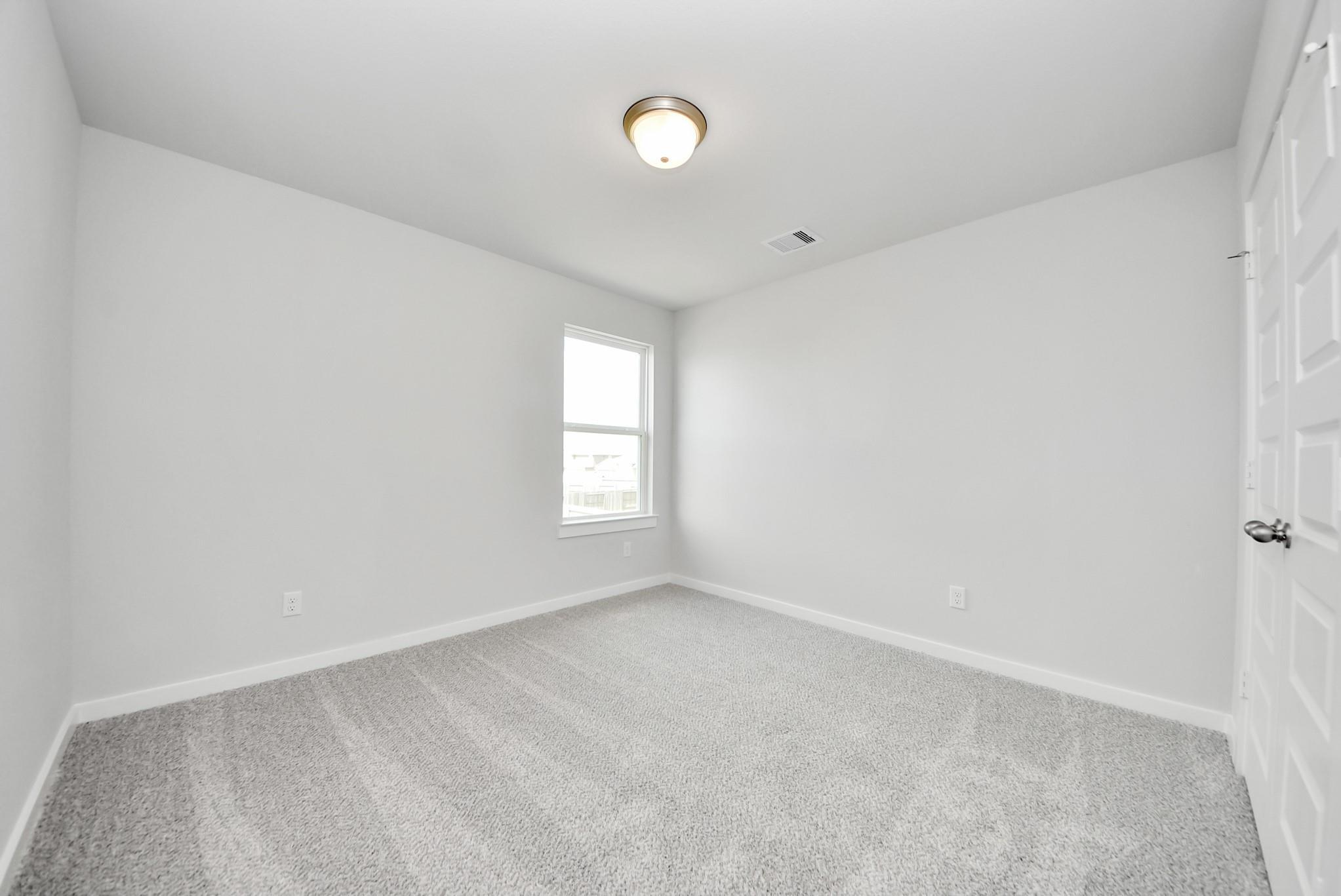 Bright, carpeted secondary bedroom with a window in The Verano B floor plan by Davidson Homes in Sunterra, Katy, Texas.