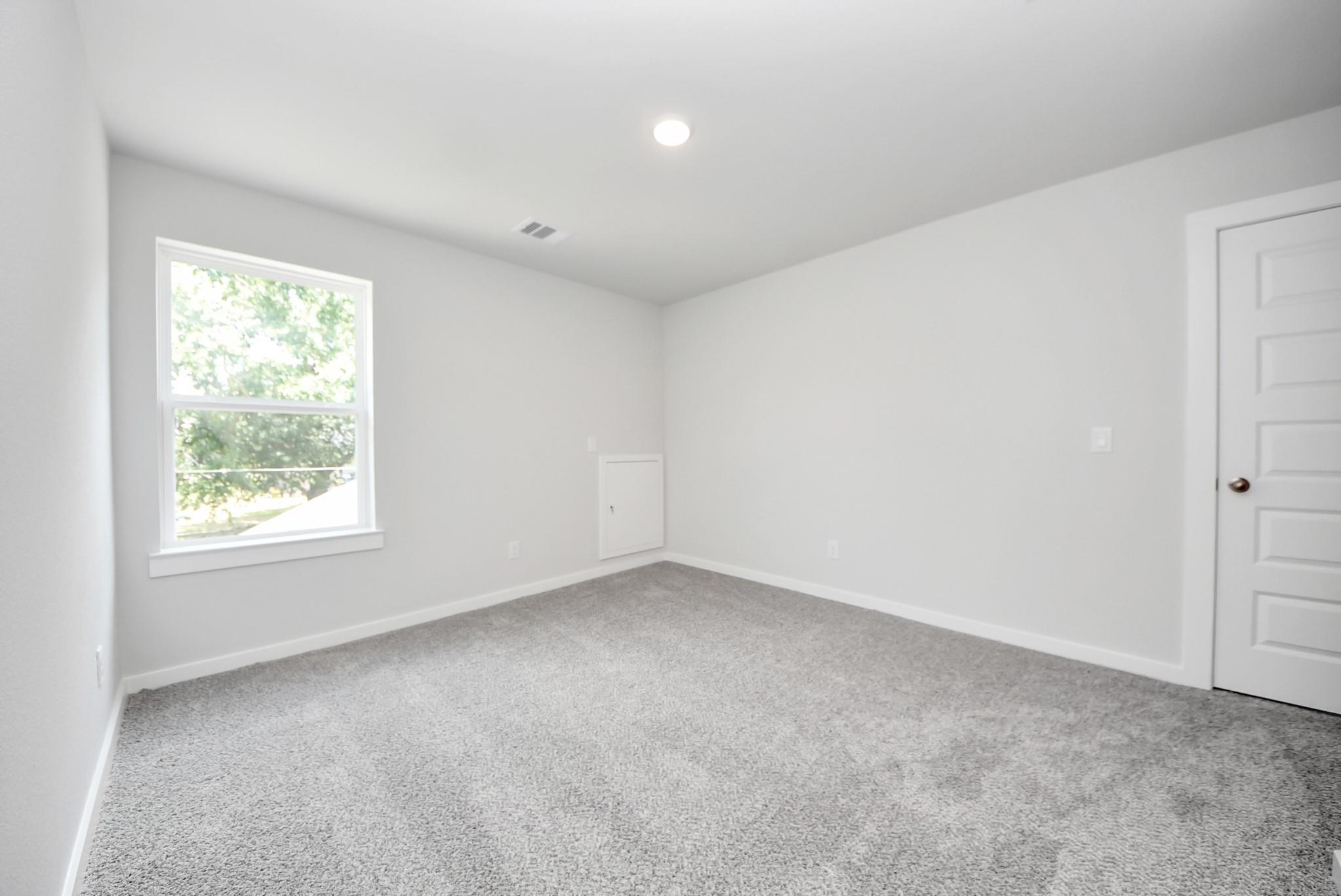 Bright, carpeted bedroom with neutral walls in The Sabine E floor plan at Windmill Estates, Magnolia, Texas.