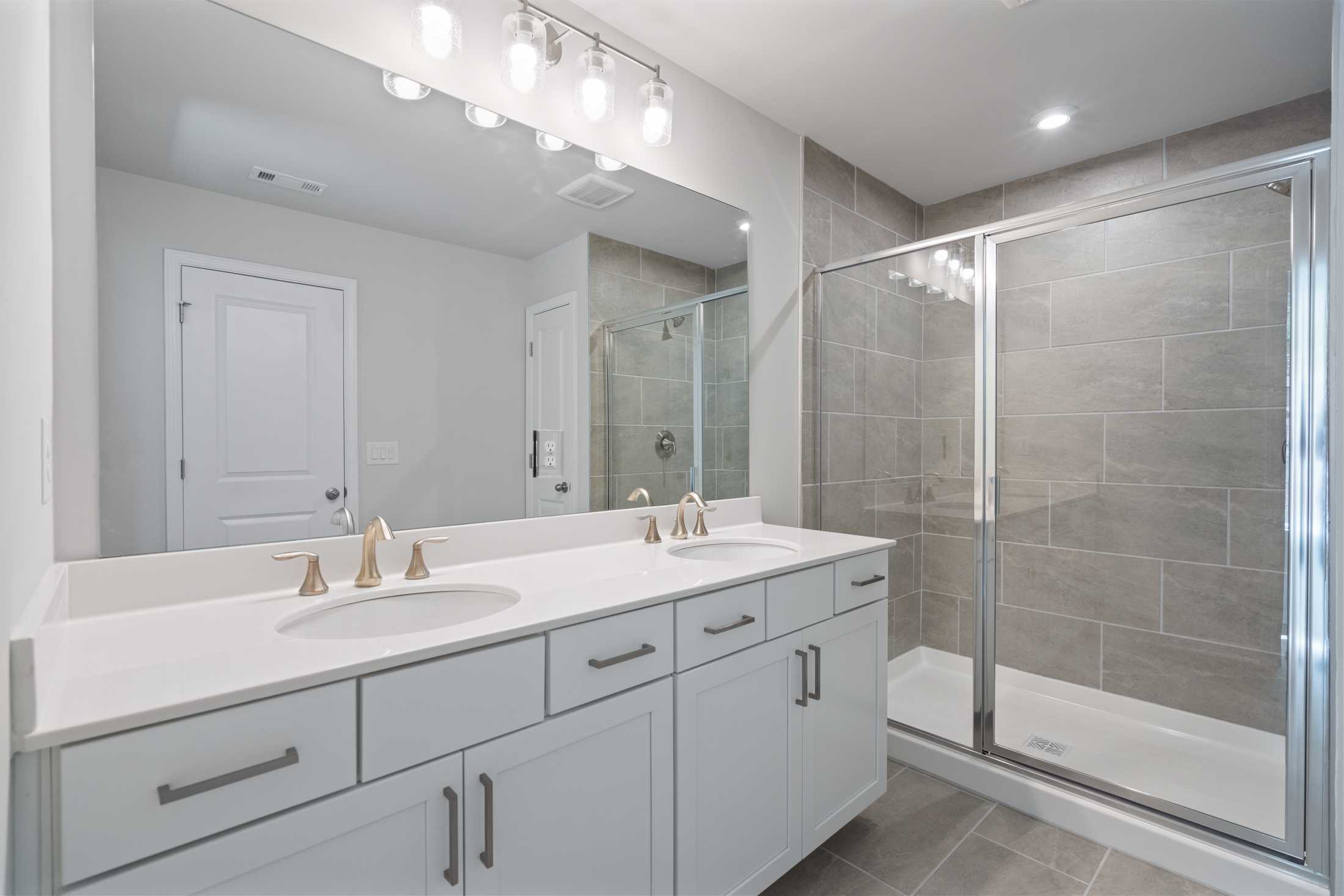 Modern master bathroom in The Cary A by Davidson Homes: double white vanity, brushed faucets, large mirrors, glass shower with gray tile