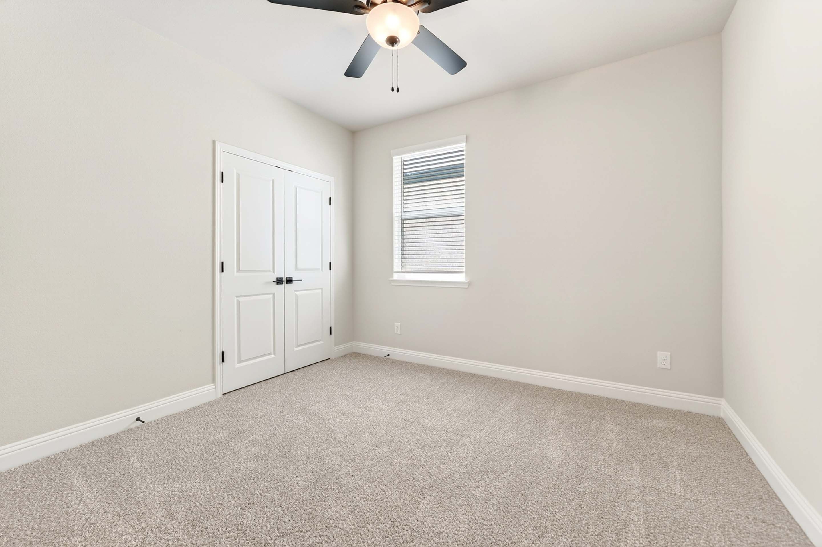 Bright secondary bedroom in The Holly home design by Davidson Homes featuring neutral carpet, closet, and ceiling fan.