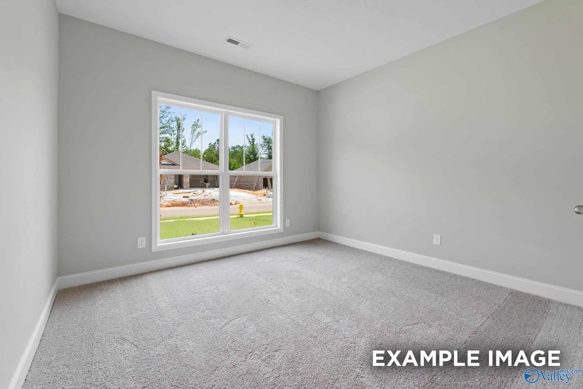 Bright secondary bedroom with gray walls, carpet flooring, and large window overlooking Lynn Meadows construction in The Everett, Meridianville, AL