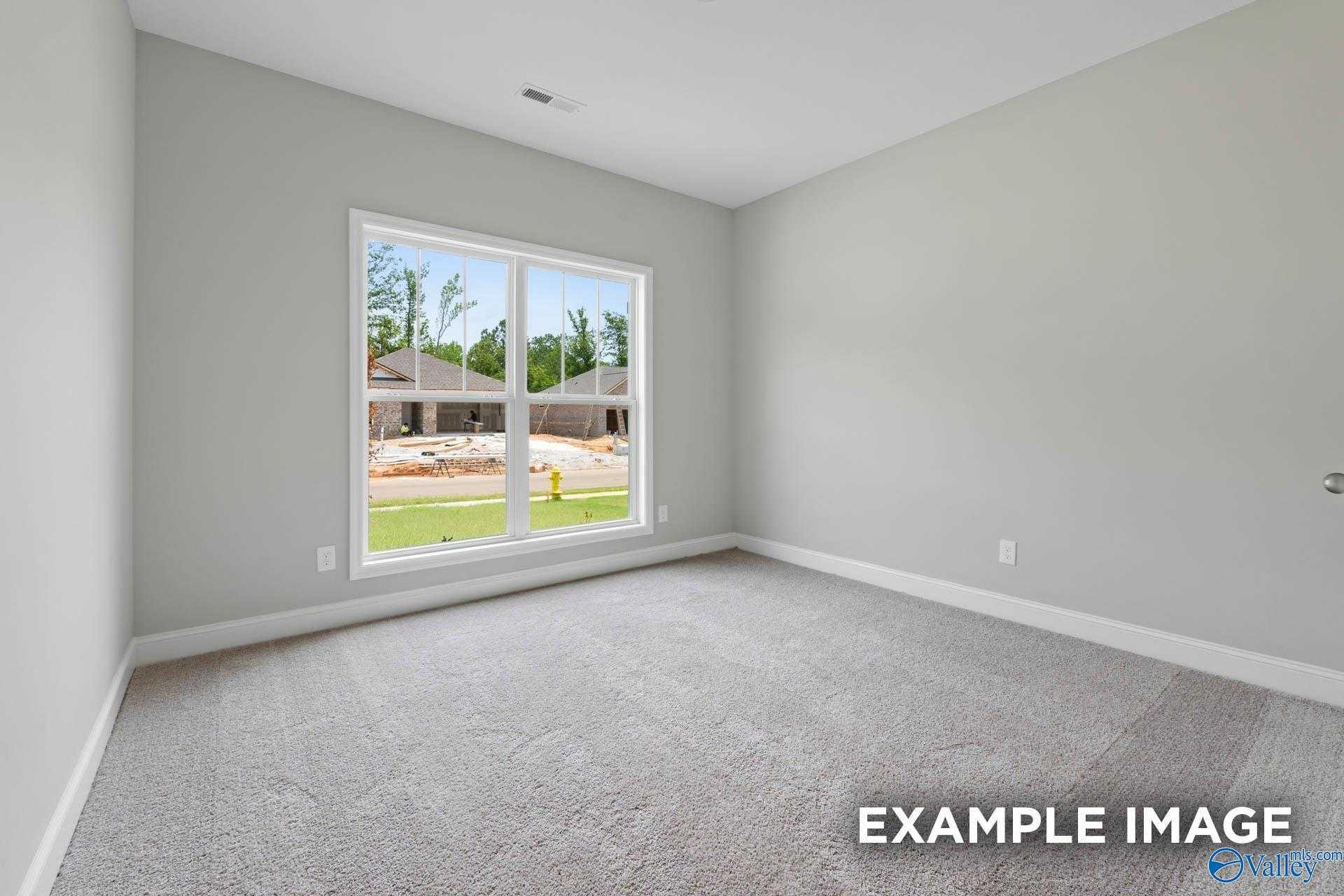Bright secondary bedroom with gray walls, carpet flooring, and large window overlooking Lynn Meadows construction in The Everett, Meridianville, AL