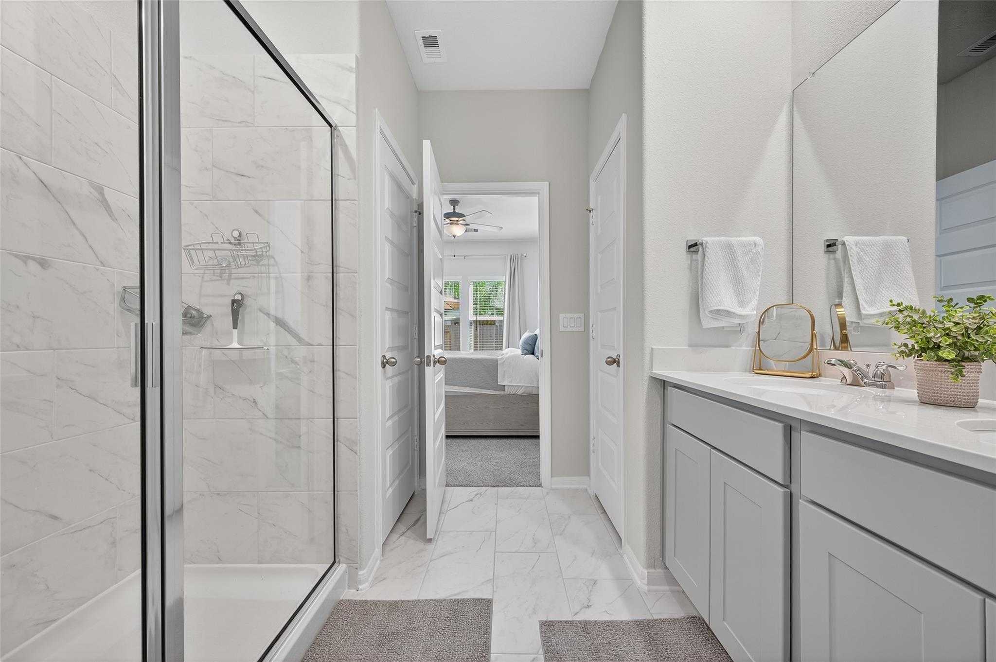 Modern master bathroom with frameless glass shower, double vanity, and bedroom access in Davidson Homes The Brazos E, Magnolia, Texas
