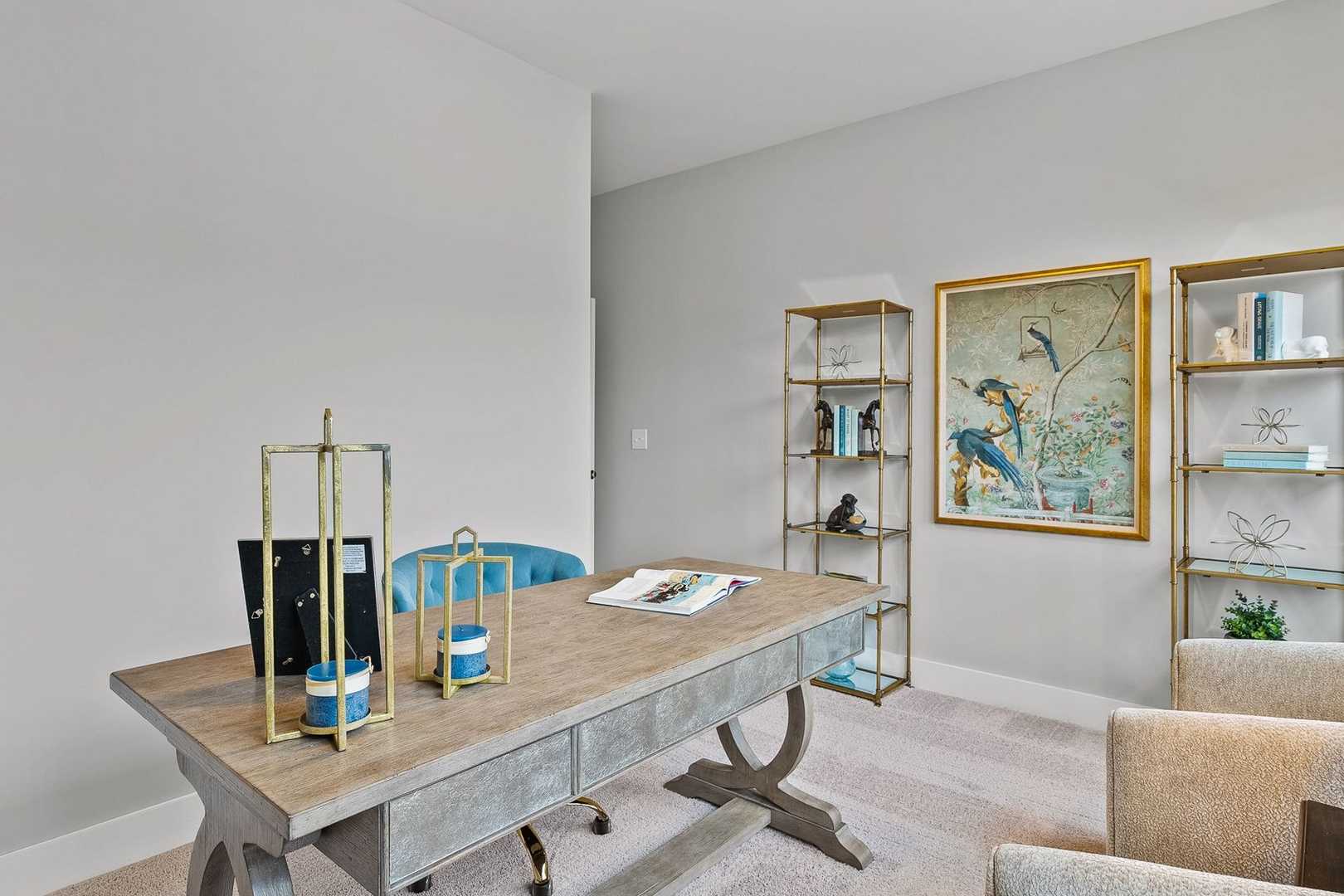 Elegant home office in The Oxford by Evermore Homes featuring wooden desk, gold-framed bird artwork, bookshelves, and beige armchairs