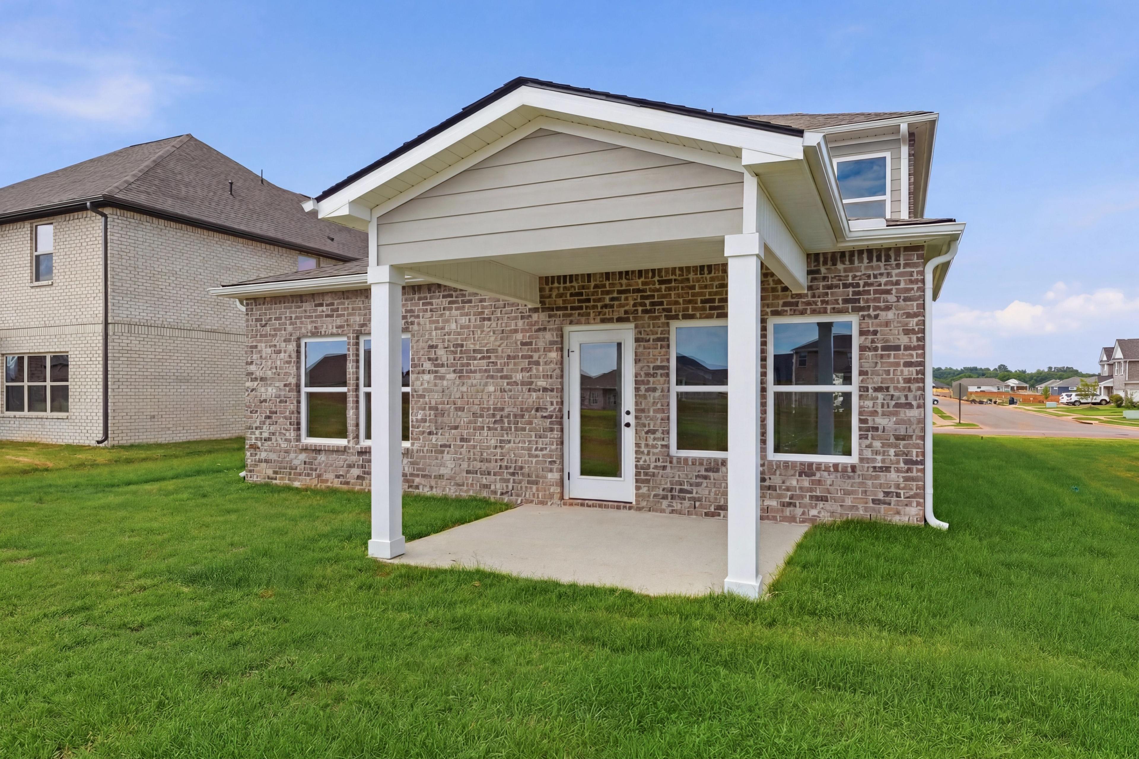 Covered rear patio of The Meadowbrook home design in Meridianville, featuring brick exterior and spacious backyard.