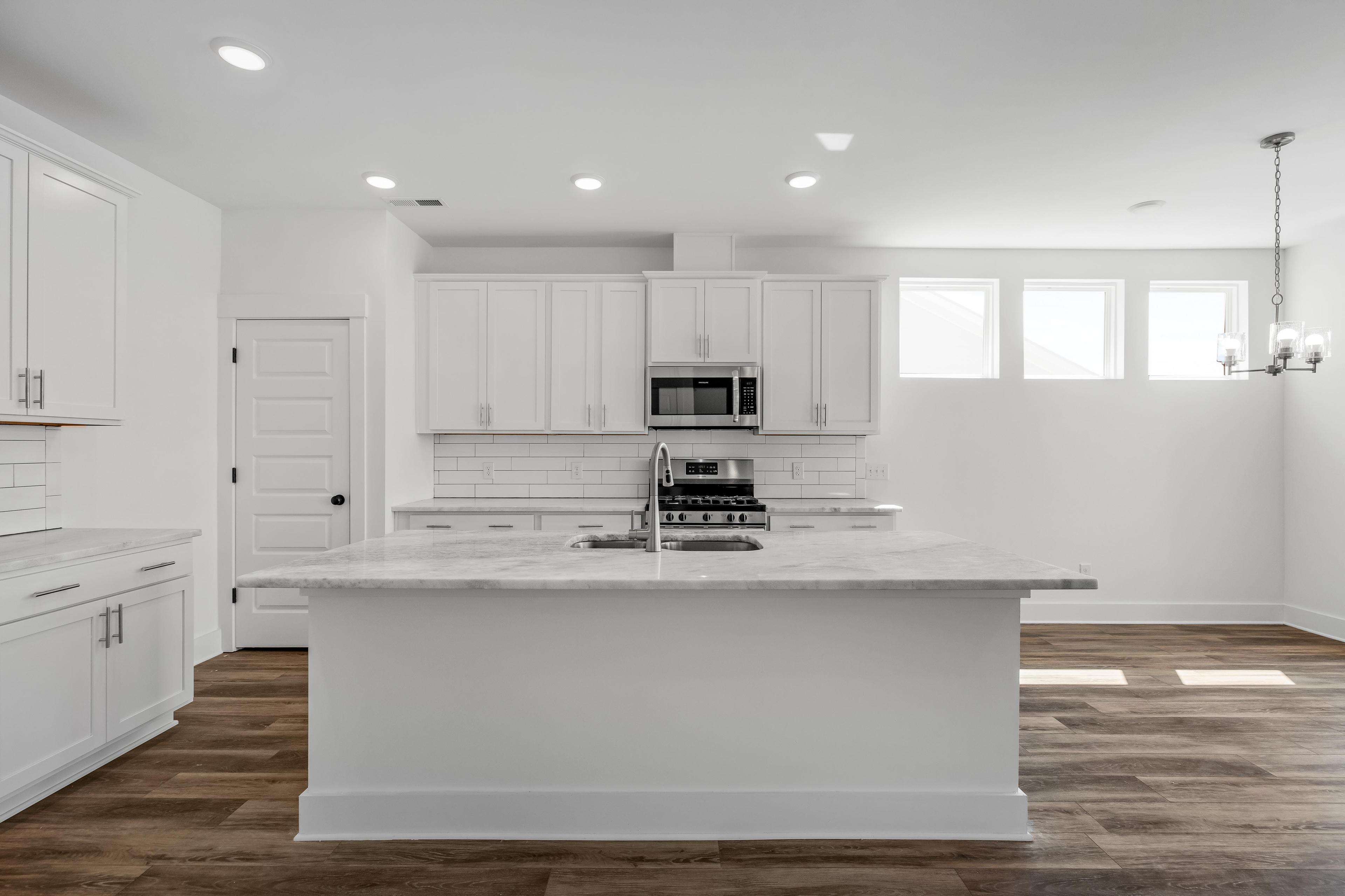 Modern white kitchen in The Cedar plan by Davidson Homes featuring a large marble island, subway tile, and wood flooring.