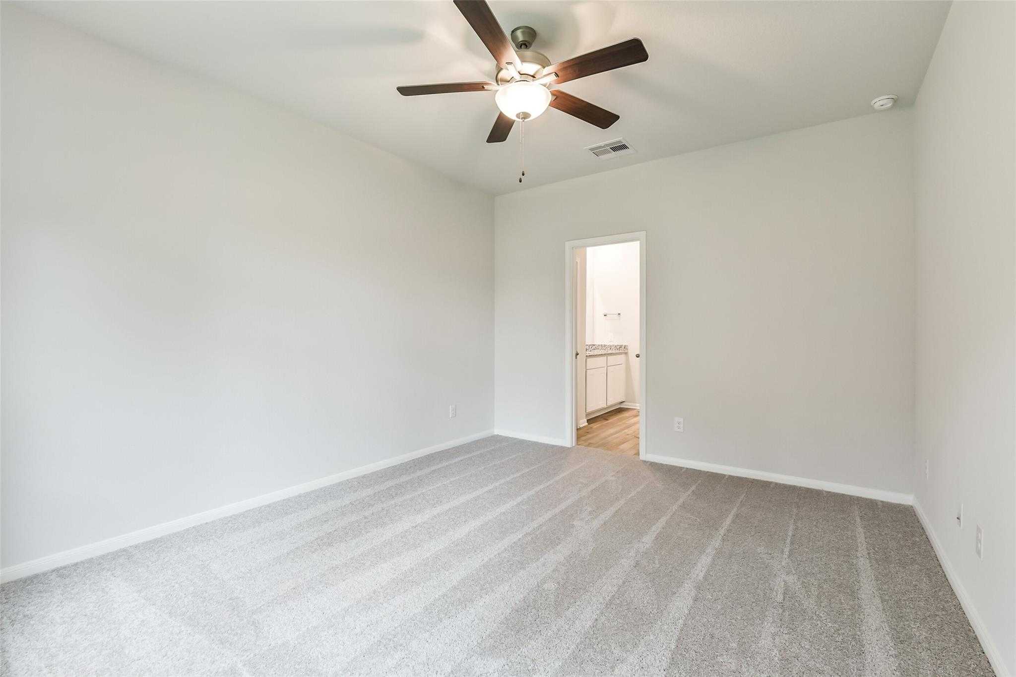 Spacious secondary bedroom featuring ceiling fan, carpeted floors, and attached bath in Davidson Homes The Brazos F, Conroe, Texas