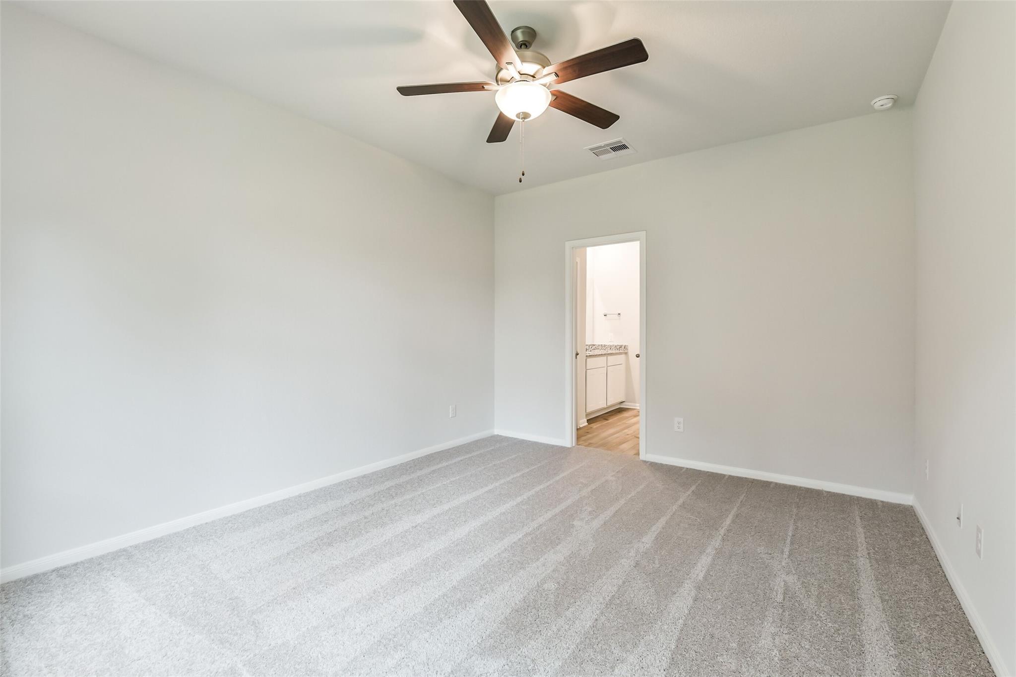 Bright bedroom with ceiling fan, neutral walls, carpet floor, and adjacent bathroom in Davidson Homes The Brazos F, Conroe, Texas