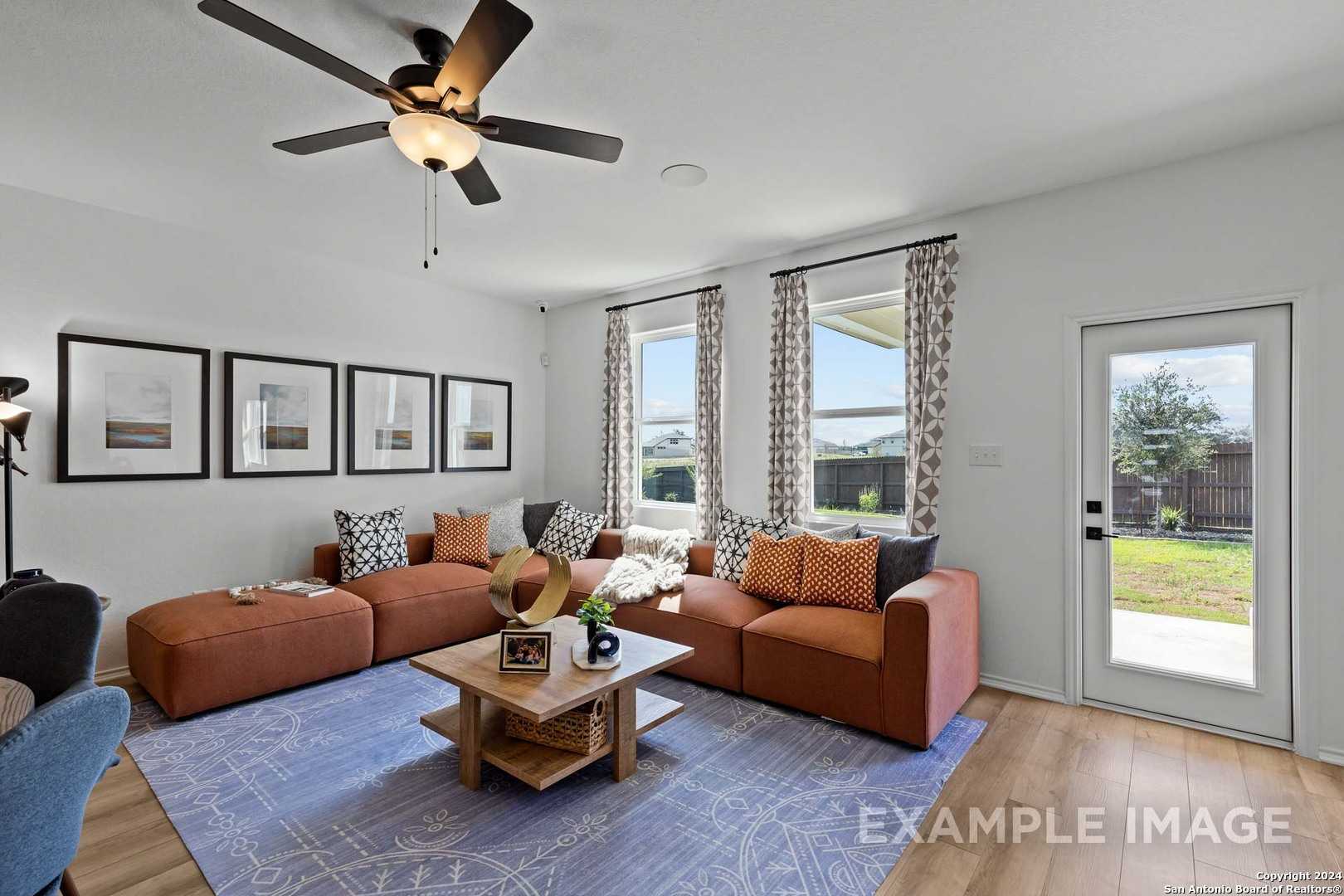 Cozy living room with L-shaped brown sectional, ceiling fan, large windows, and backyard view in 3-bedroom Davidson Homes The Douglas G, Bricewood, San Antonio