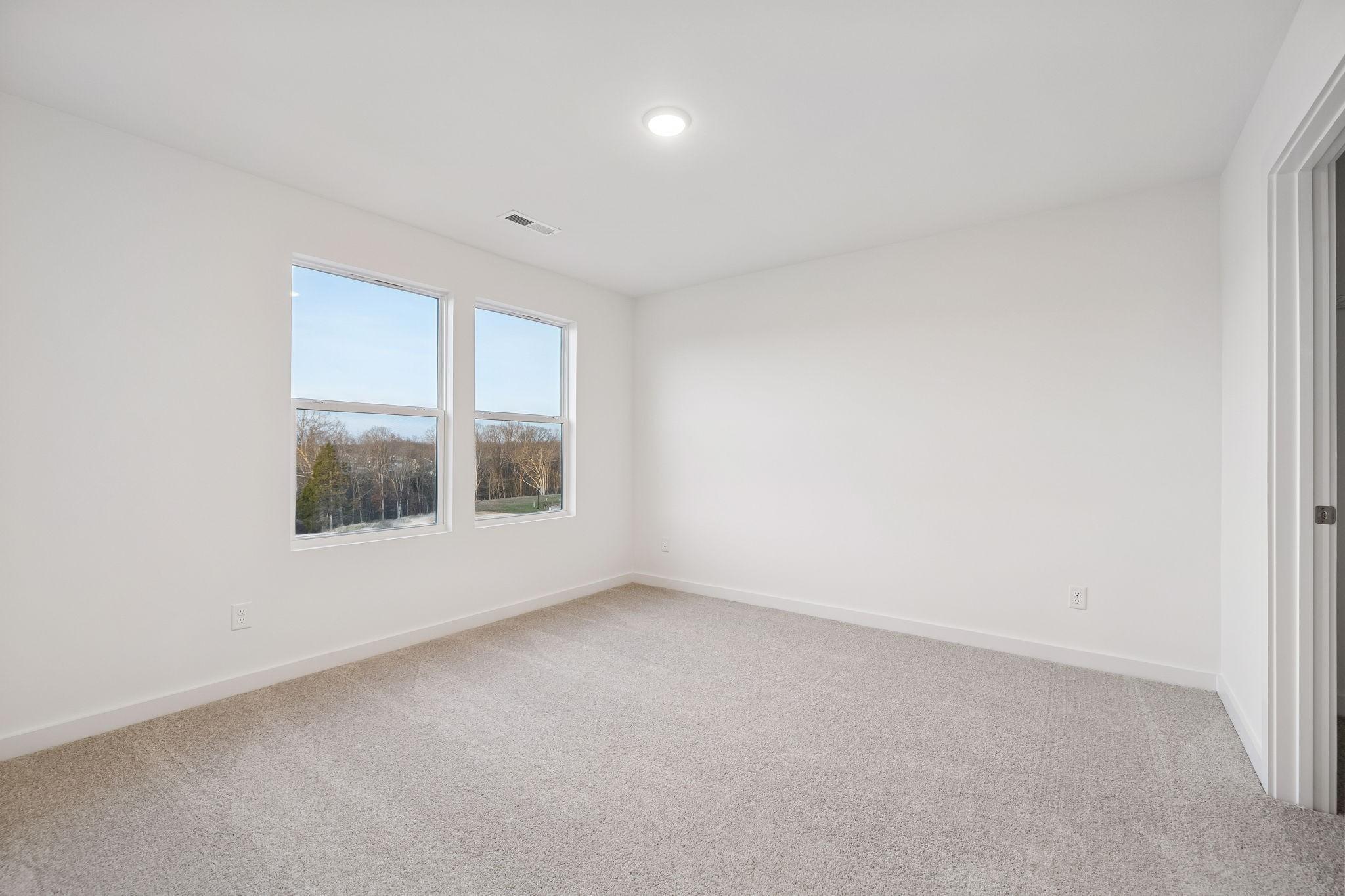 Spacious empty bedroom with large windows overlooking wooded view in Davidson Homes The Willow, Calista Farms, White House, TN