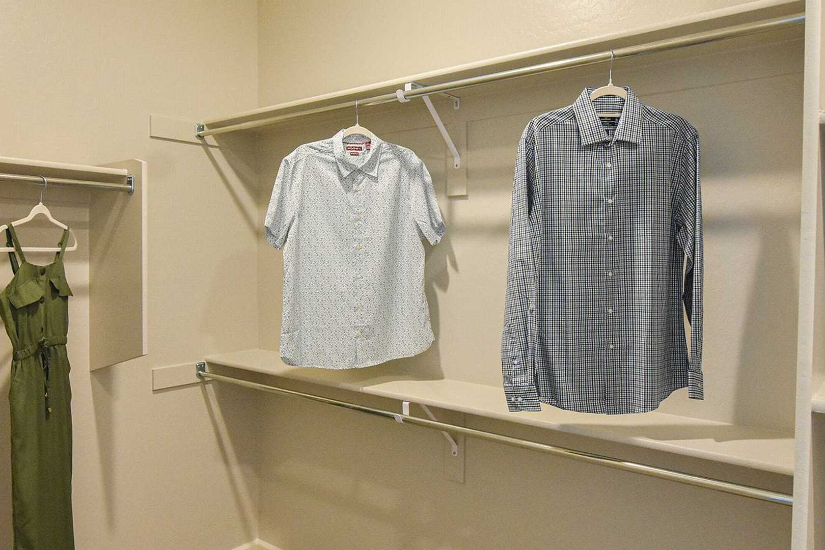 Spacious walk-in closet in The Summit B master suite with hanging green sundress, white shirts, and plaid button-down on beige shelves