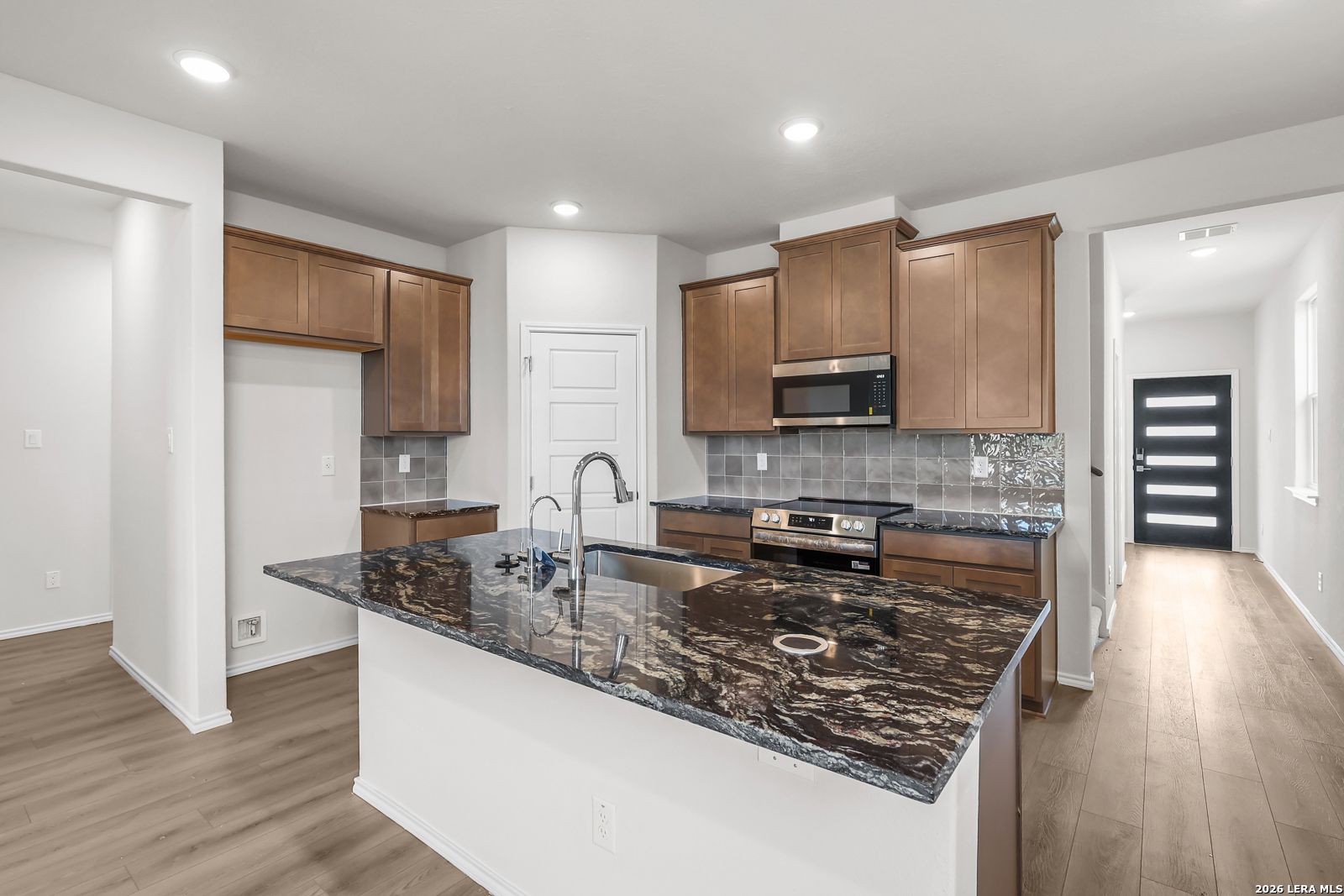 Modern kitchen with granite island and wood cabinets in The San Marcos F floor plan, Rayburn Valley, San Antonio, Texas.
