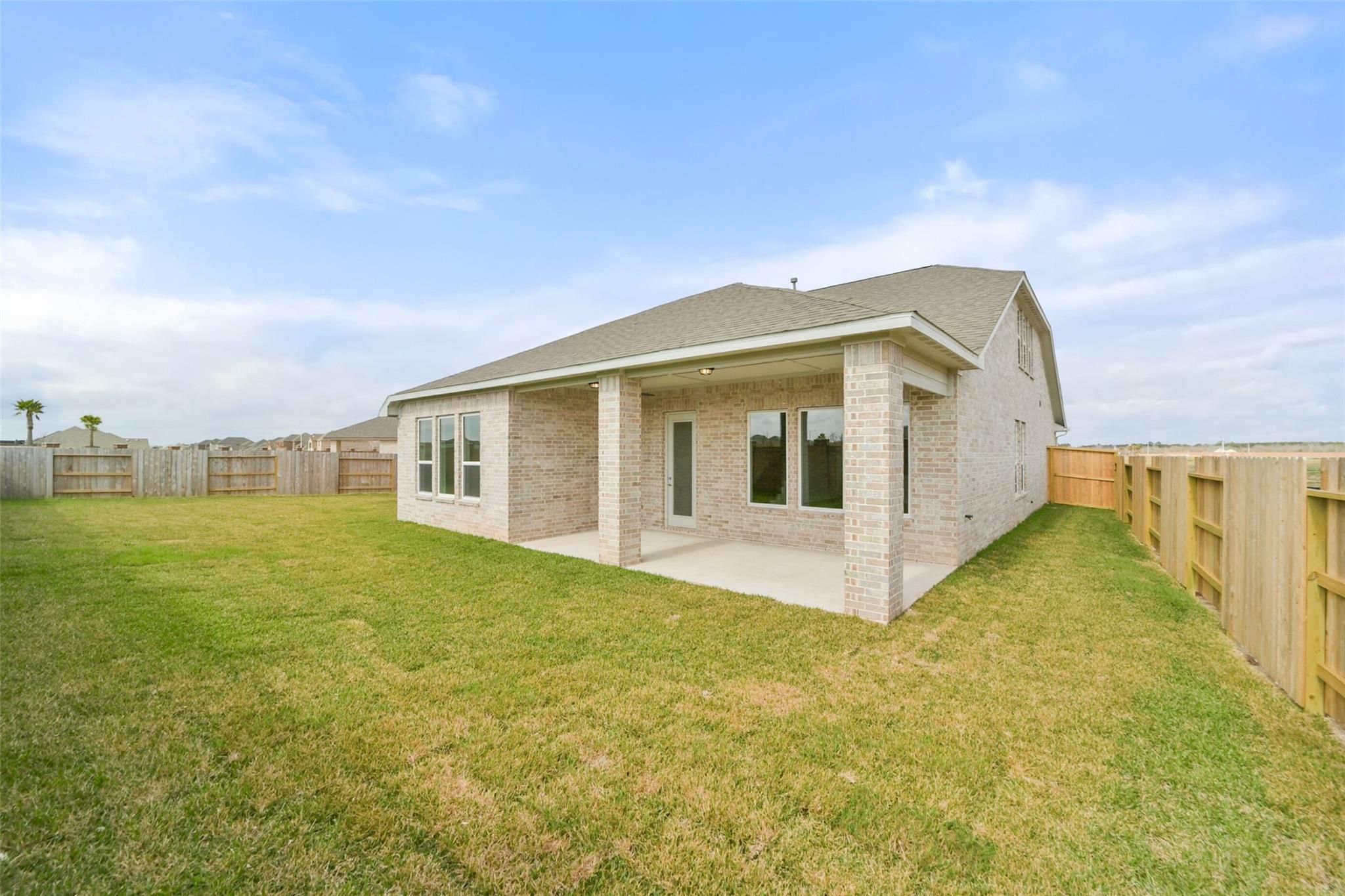 Two-story beige brick home with covered side patio, large windows, and fenced green yard in Lago Mar, Texas City - Davidson Homes Zion A