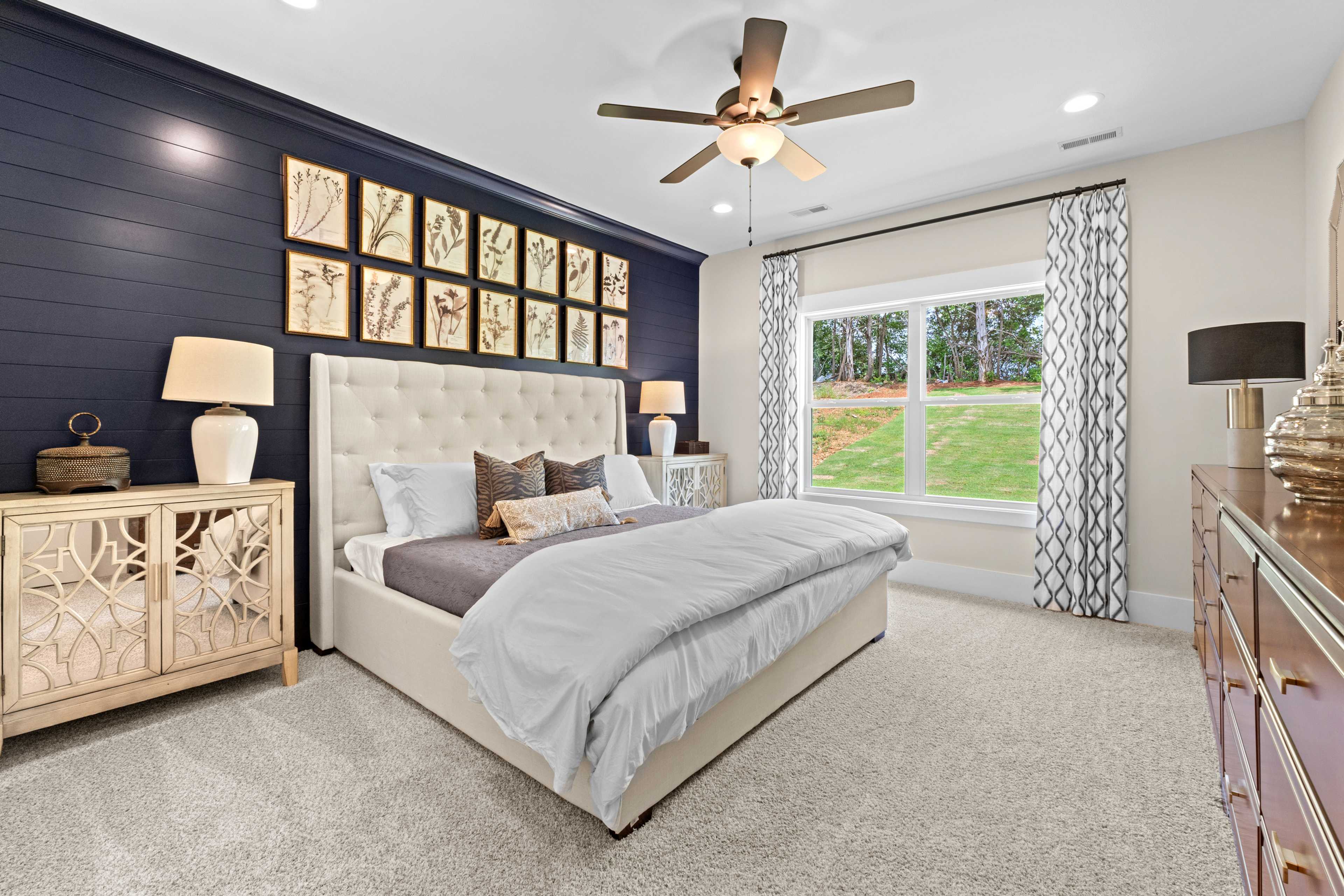 Spacious master bedroom in Ivy Hills Toney Alabama with navy shiplap wall, botanical art, king bed, ceiling fan and lawn view