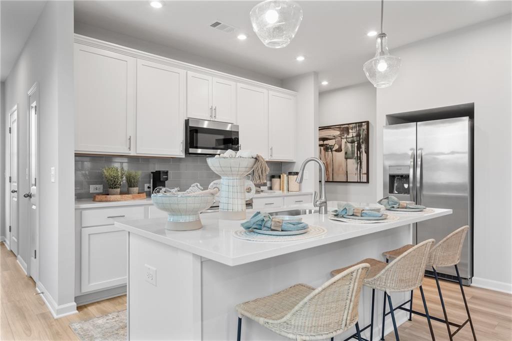 White kitchen island with pendant lights, bar seating, and stainless appliances in Davidson Homes Wilmington B plan, Emerson, GA