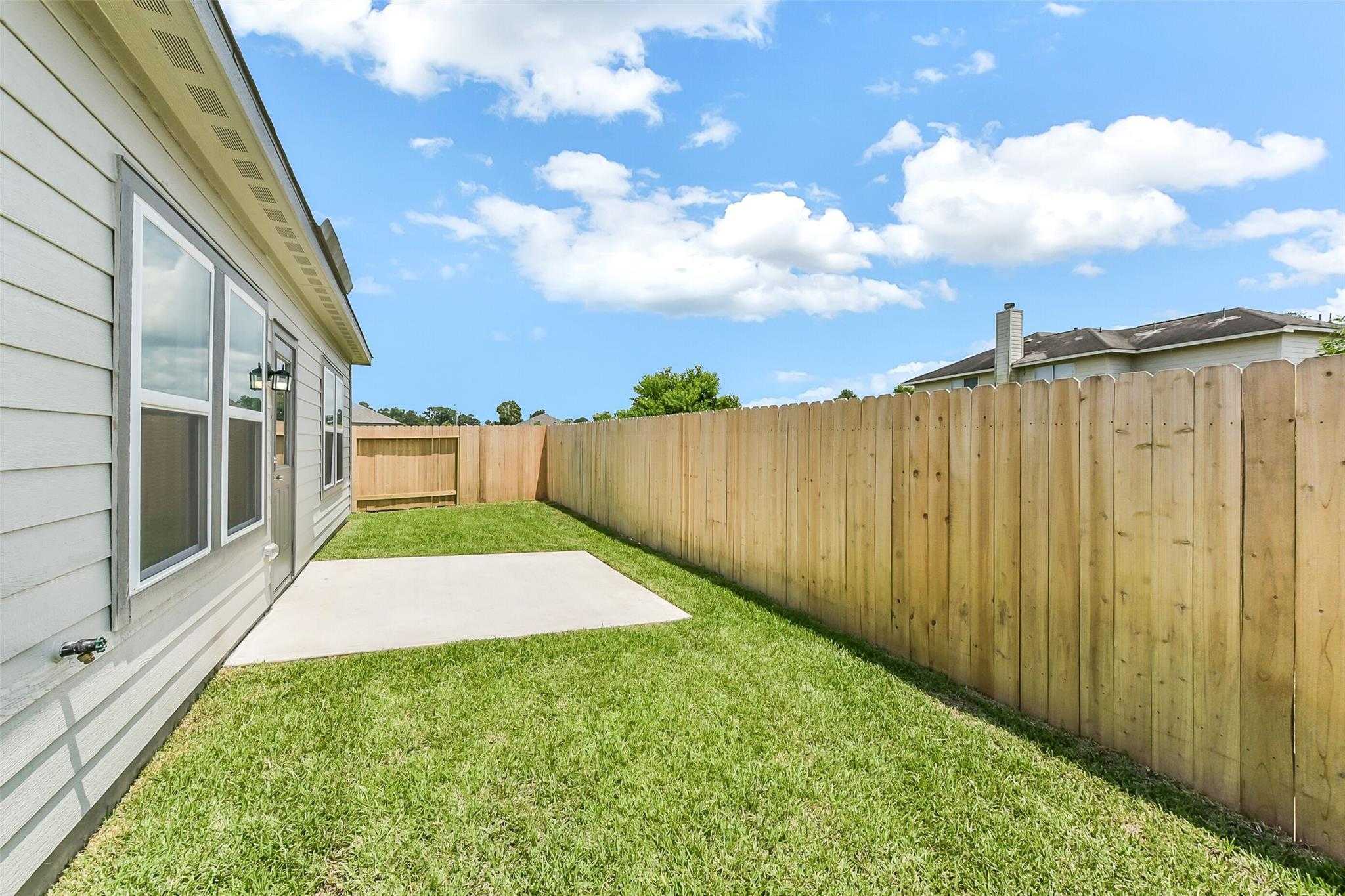 Exterior side of Davidson Homes The Frio F with concrete patio, lush green lawn, and wooden privacy fence in Dayton, Texas