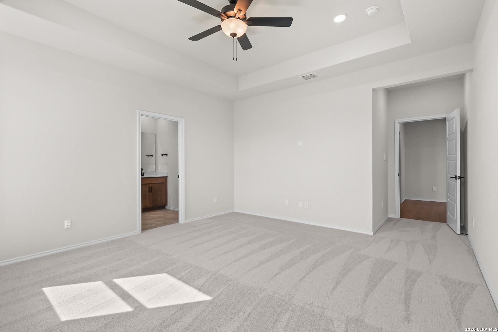 Spacious primary bedroom with tray ceiling, ceiling fan, and carpet flooring in Davidson Homes Glenwood E plan, San Antonio, TX