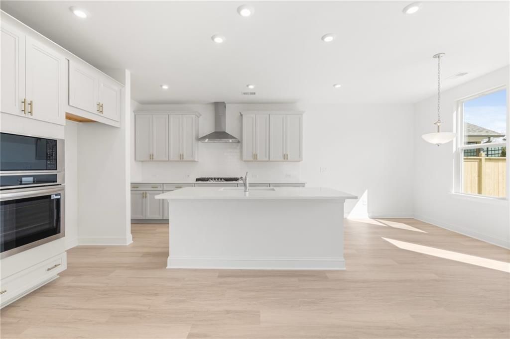 Modern white kitchen with large island, stainless steel appliances, and hardwood floors in Davidson Homes The Gavin E, Kennesaw, GA
