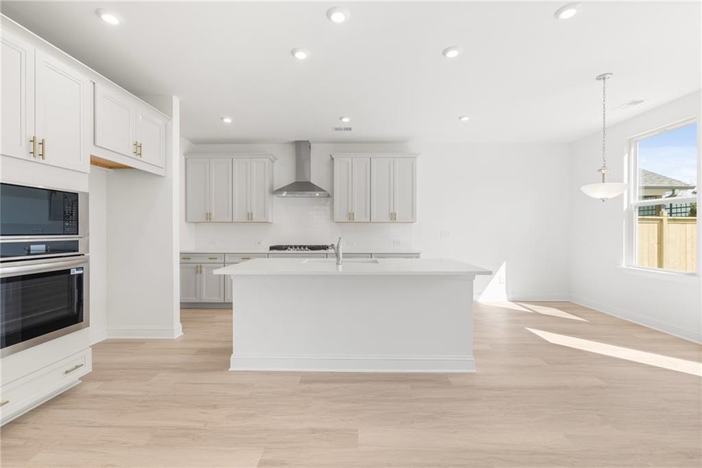 Modern white kitchen with large island, stainless steel appliances, and hardwood floors in Davidson Homes The Gavin E, Kennesaw, GA