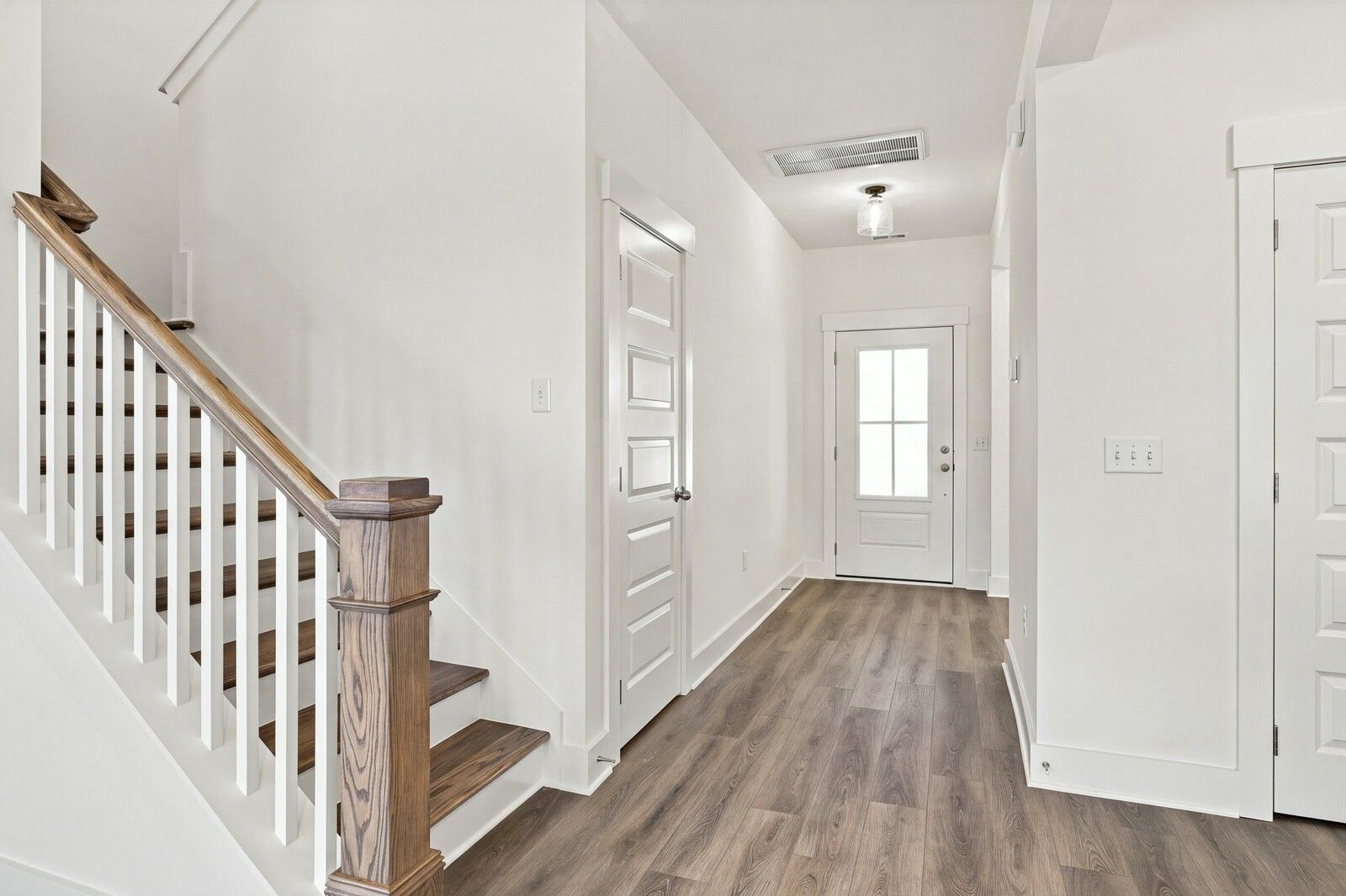 Bright foyer with wood-look flooring, white front door, and staircase in Davidson Homes The Willow B, Gallatin, Tennessee