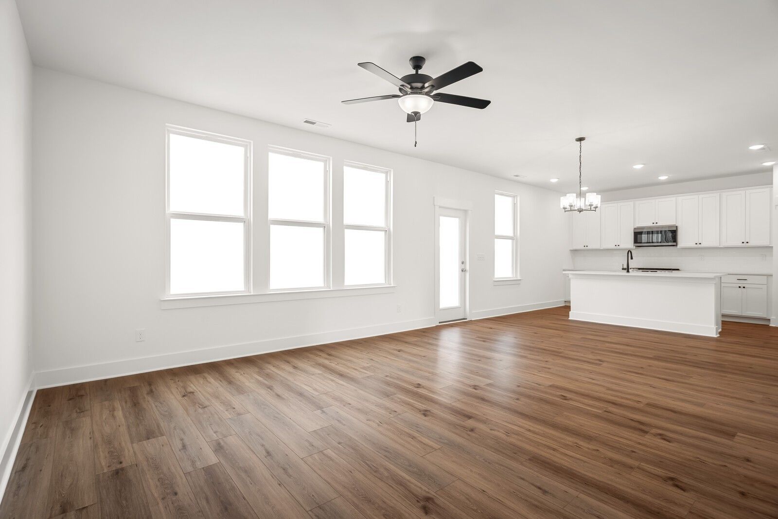 Bright open kitchen with white cabinets, stainless appliances, large island, and hardwood floors in The Logan C by Davidson Homes, Gallatin, TN