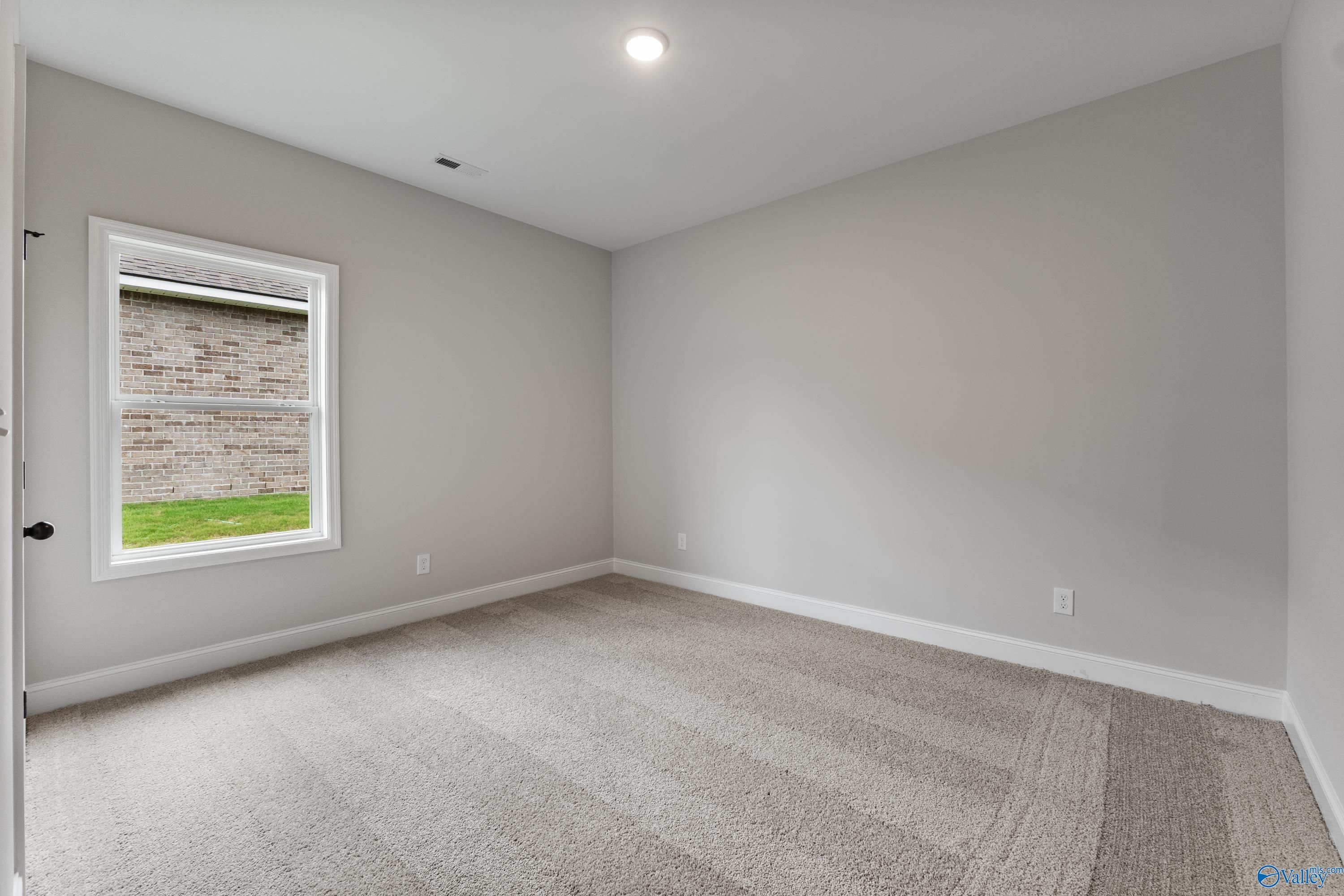 Bright secondary bedroom with gray walls, carpet floor, and large window in Davidson Homes The Daphne, Huntsville AL