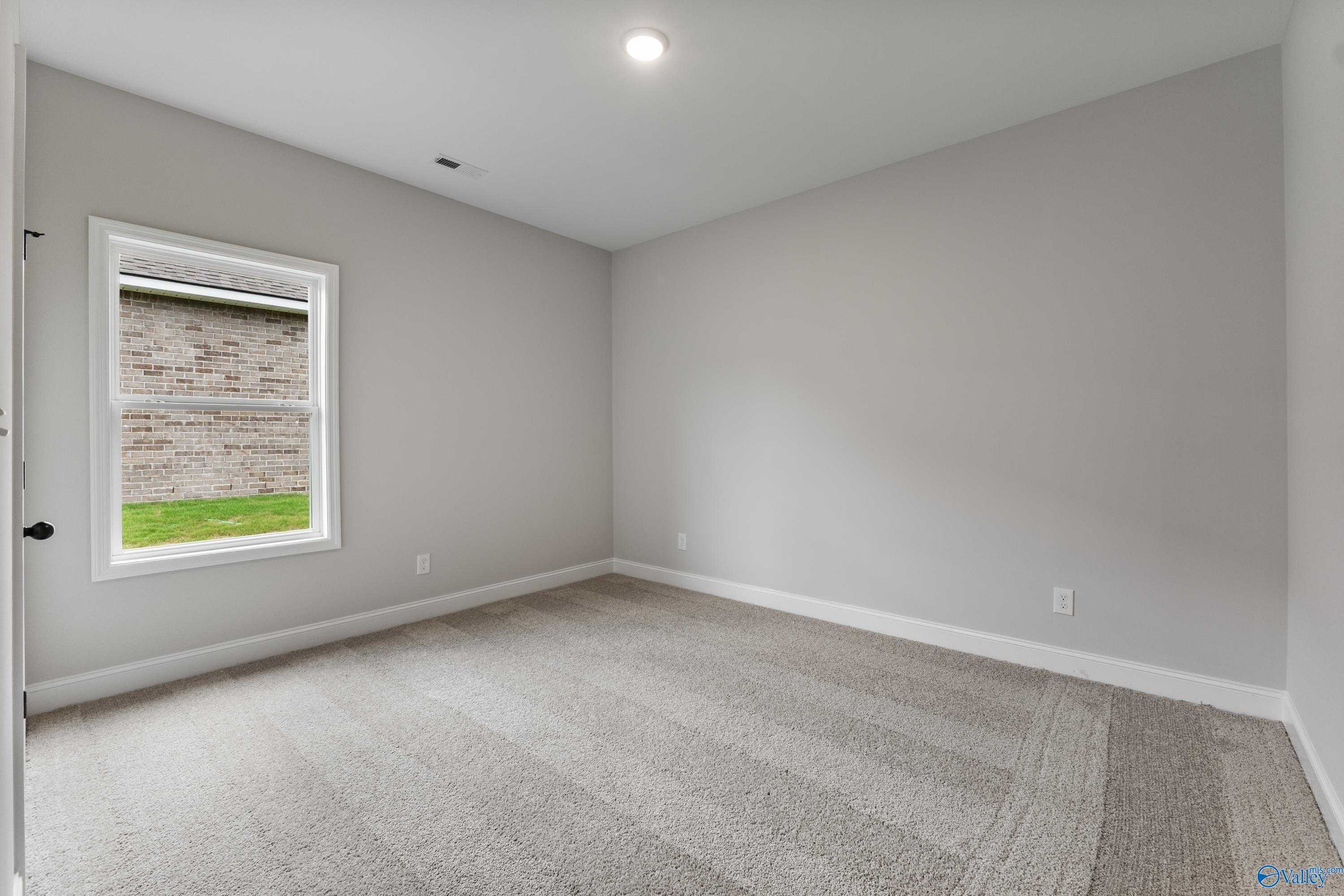 Bright secondary bedroom with gray walls, carpet floor, and large window in Davidson Homes The Daphne, Huntsville AL