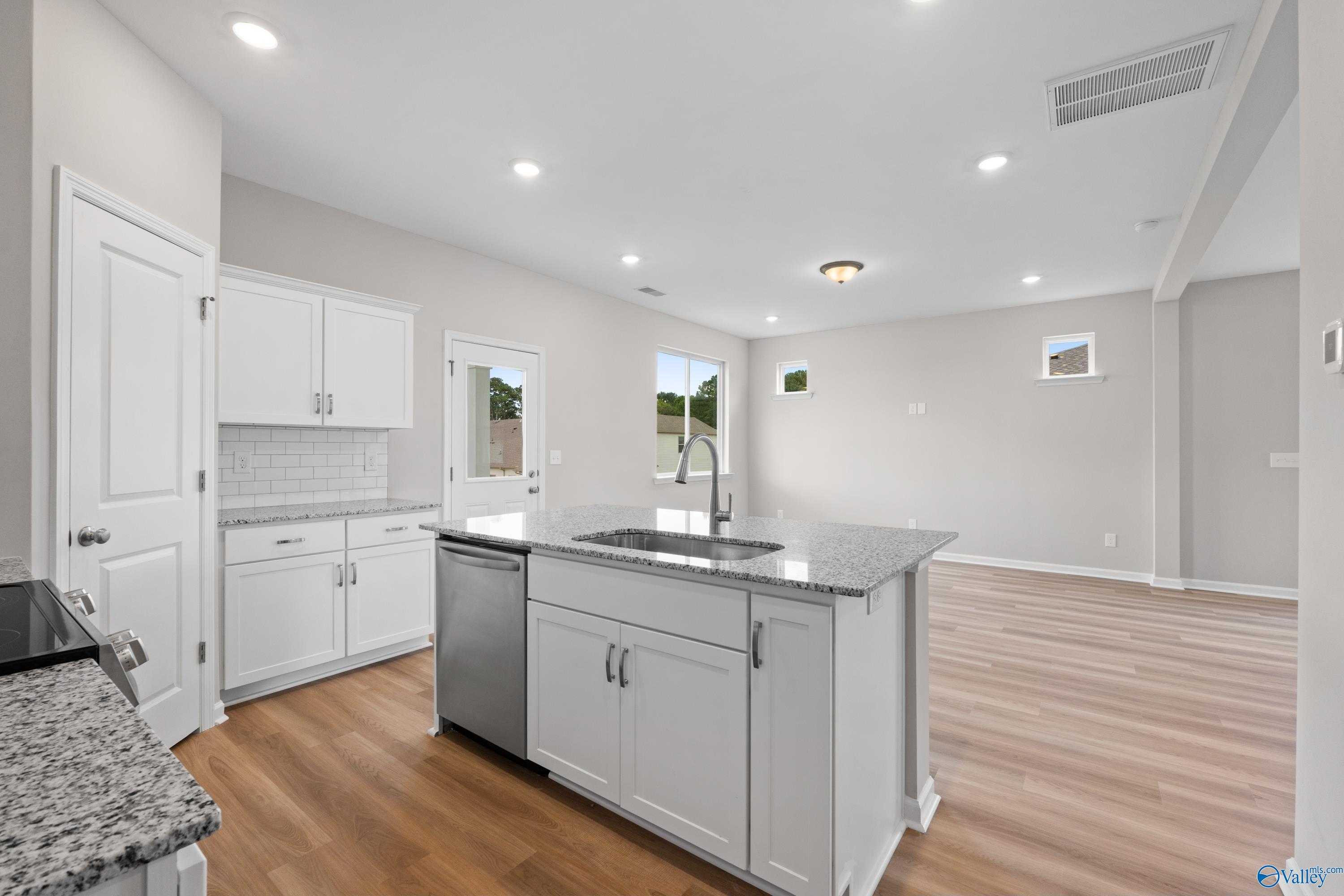 Modern kitchen featuring white shaker cabinets, granite island with sink, stainless dishwasher in The Augusta by Evermore Homes, Madison AL