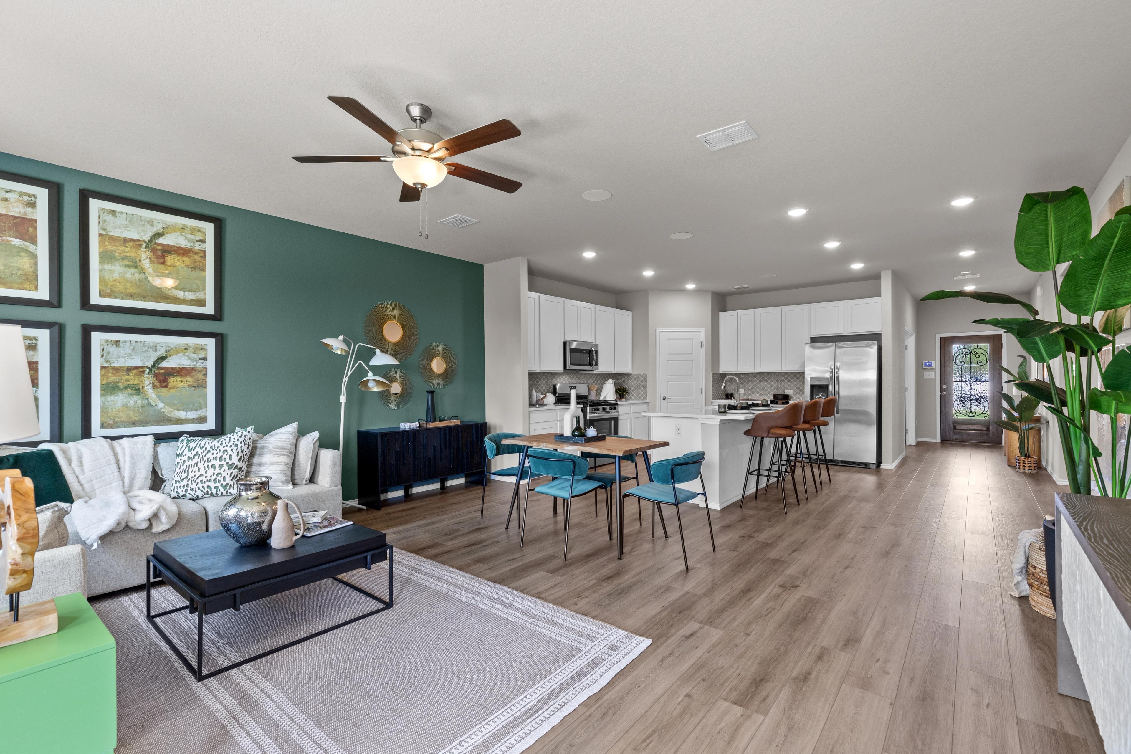 Open-concept living room and kitchen in Comanche Ridge San Antonio TX with green accent wall, hardwood floors, and modern island seating