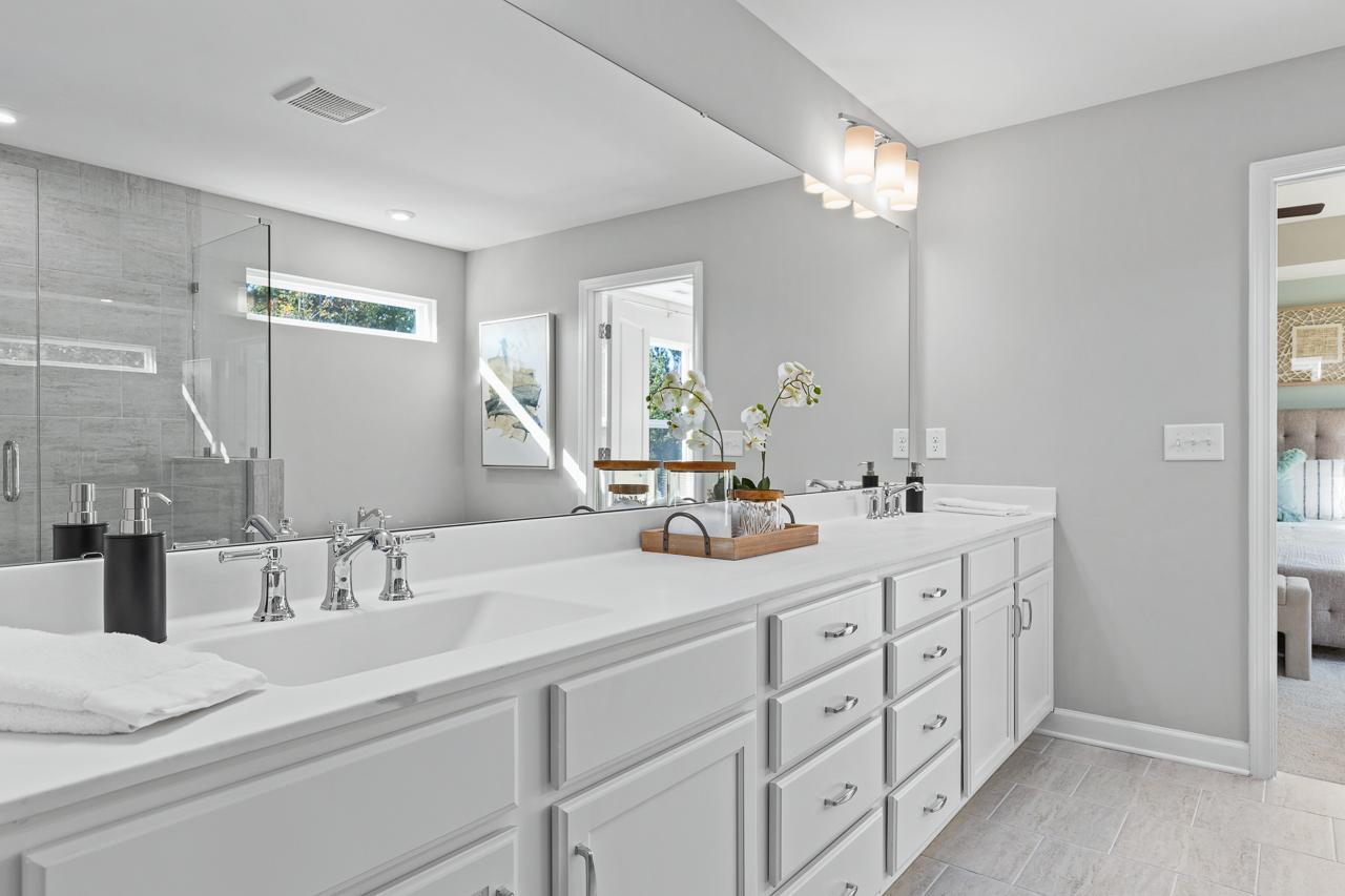Modern master bathroom in The Hemlock featuring a dual vanity with white cabinets, quartz countertops, and glass shower.