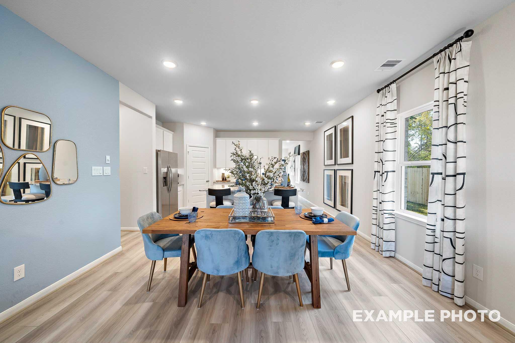 Spacious dining room in The San Marcos floor plan with wooden table, blue velvet chairs, floral centerpiece, and open kitchen view