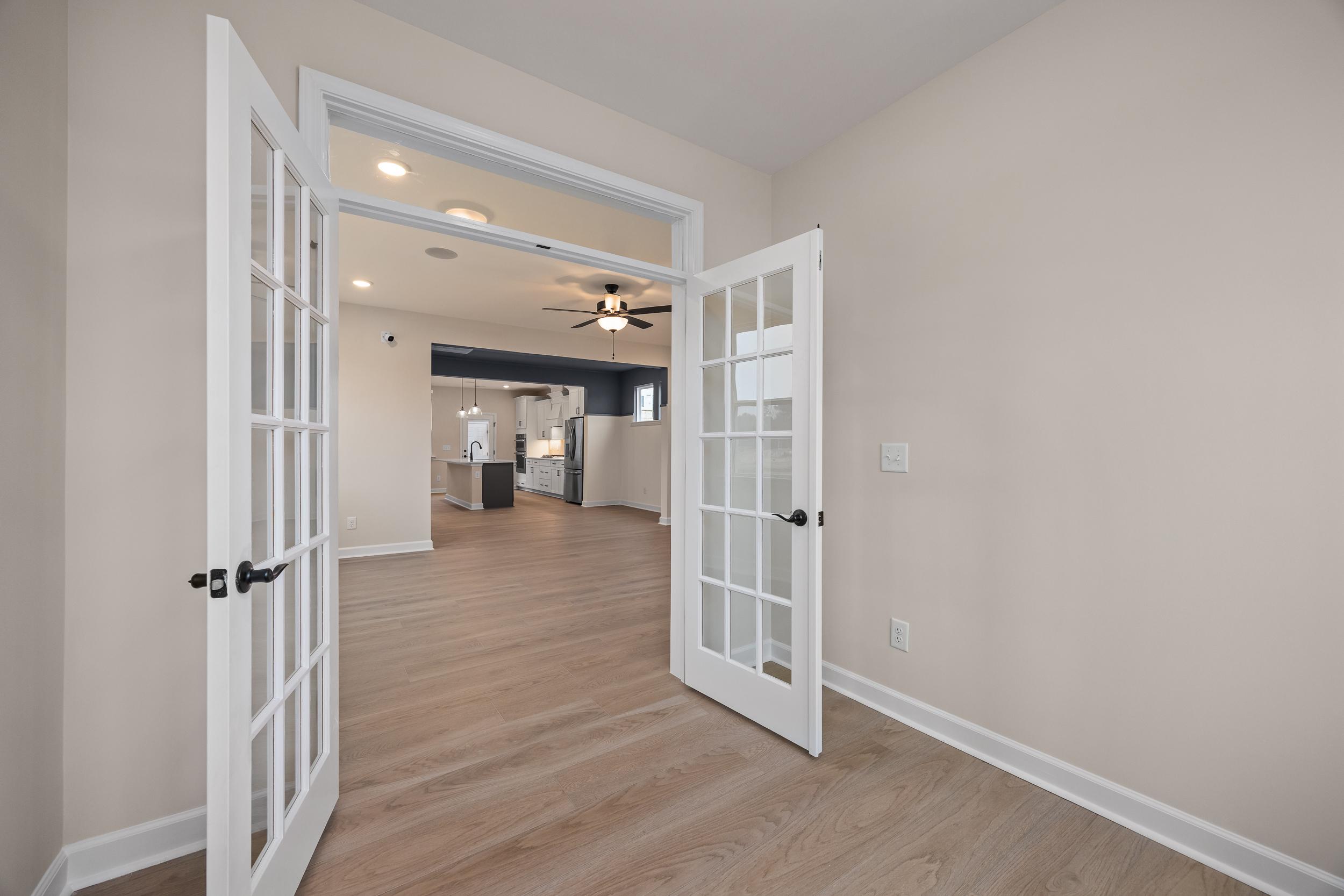 Open French doors revealing modern kitchen in Forestville Yard home by Davidson Homes, Knightdale NC, with hardwood floors and dark cabinetry