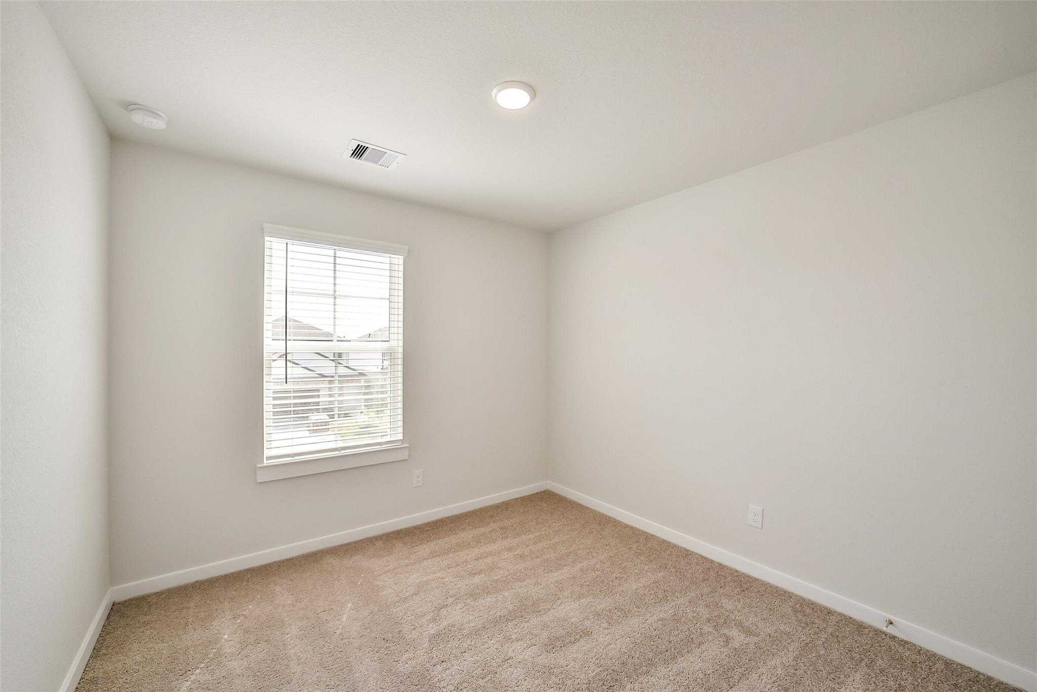 Empty bedroom with beige walls, carpet flooring, and window blinds in Davidson Homes The Blanco E, Magnolia, Texas