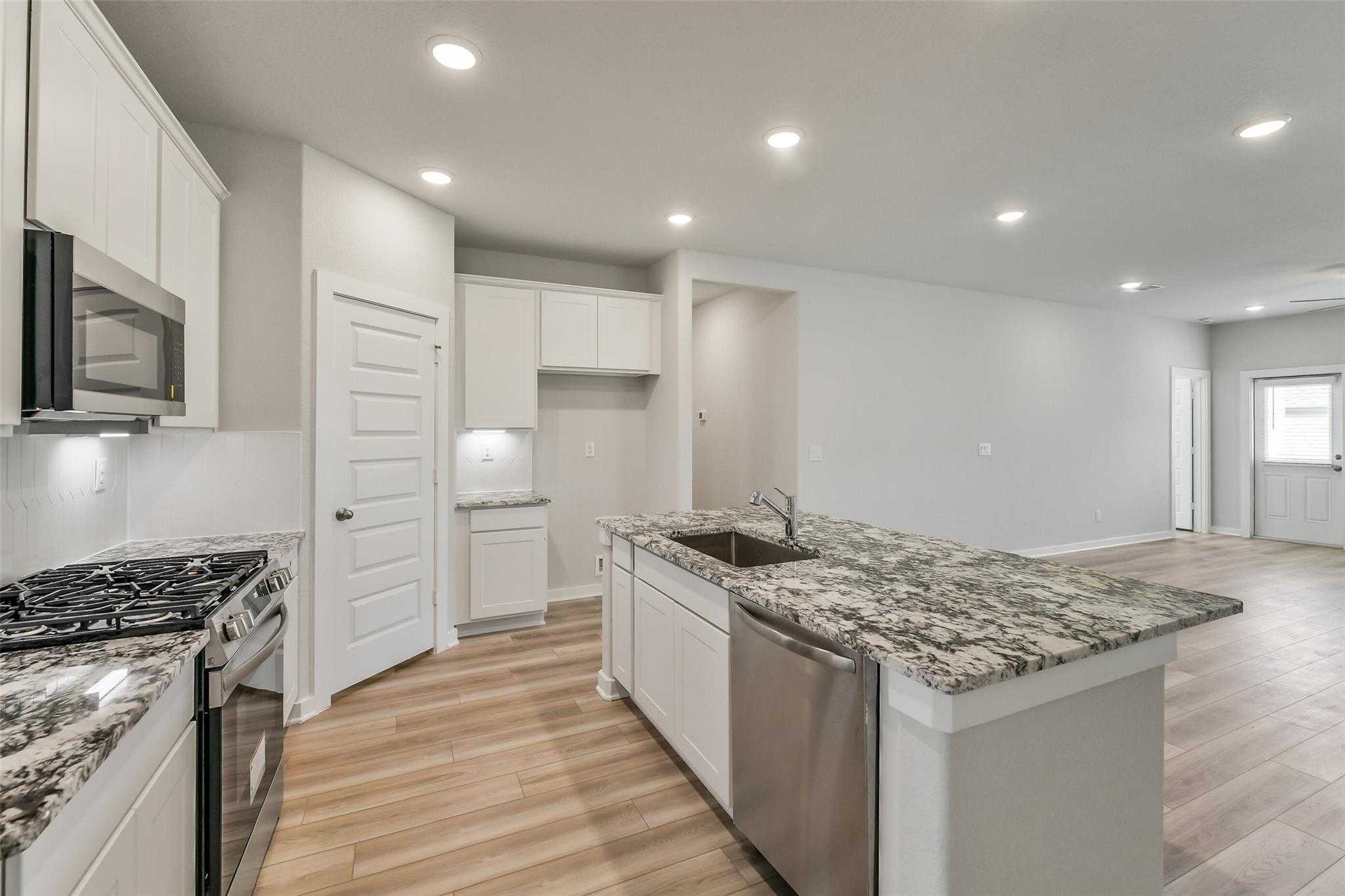 Open-concept kitchen with granite countertops, white cabinets, stainless appliances in The Rio Grande H by Davidson Homes, Magnolia TX