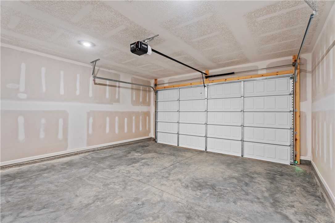 Empty one-car garage with white sectional door, overhead opener, and concrete floor in Evermore Homes The Orion, Cusseta, Alabama