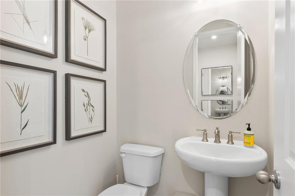 Elegant powder room featuring pedestal sink, round mirror, and botanical prints in Davidson Homes The Danbury C, Buford, Georgia