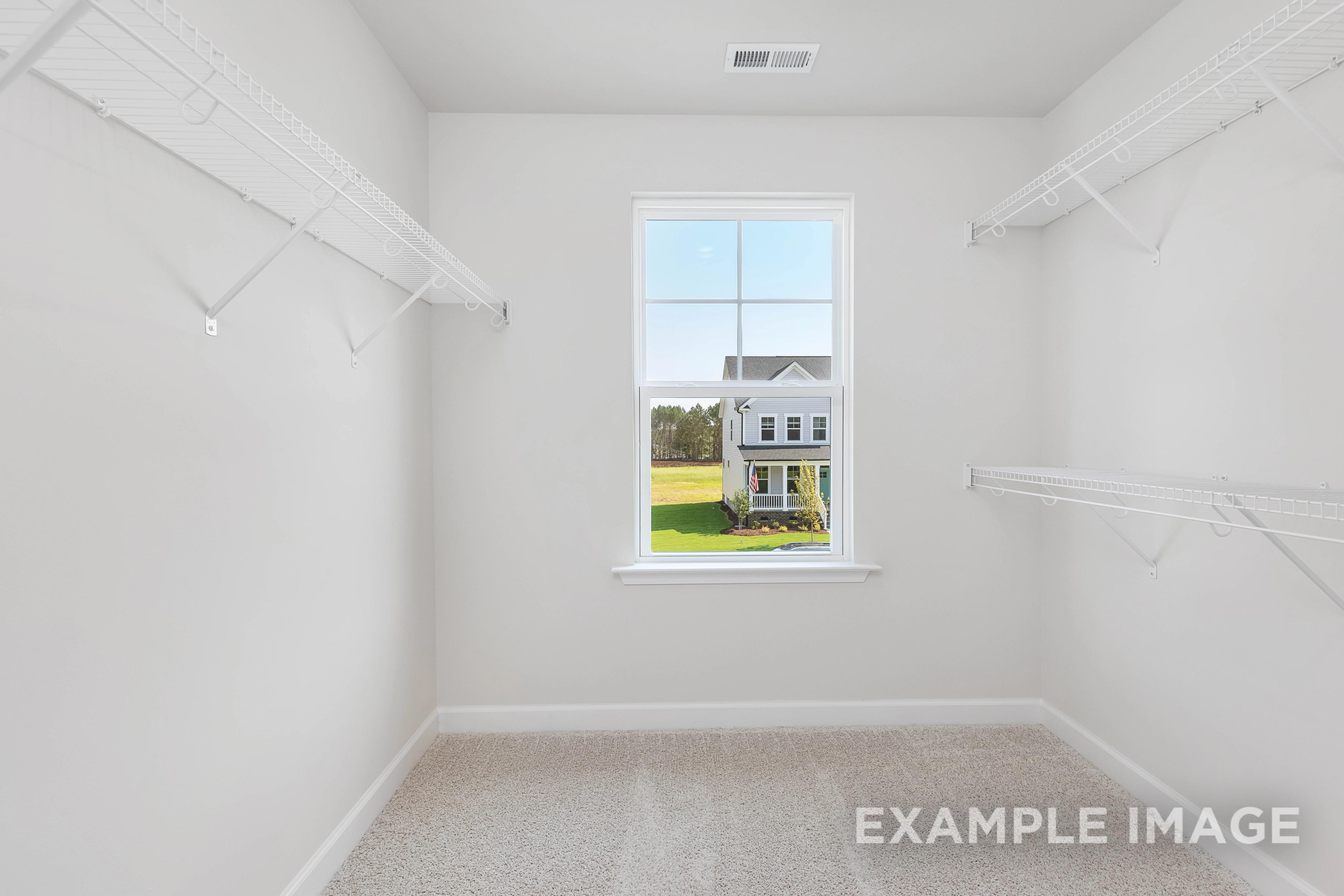 Spacious walk-in closet in The Willow B master suite featuring white shelving, rods, and window overlooking green lawn and home
