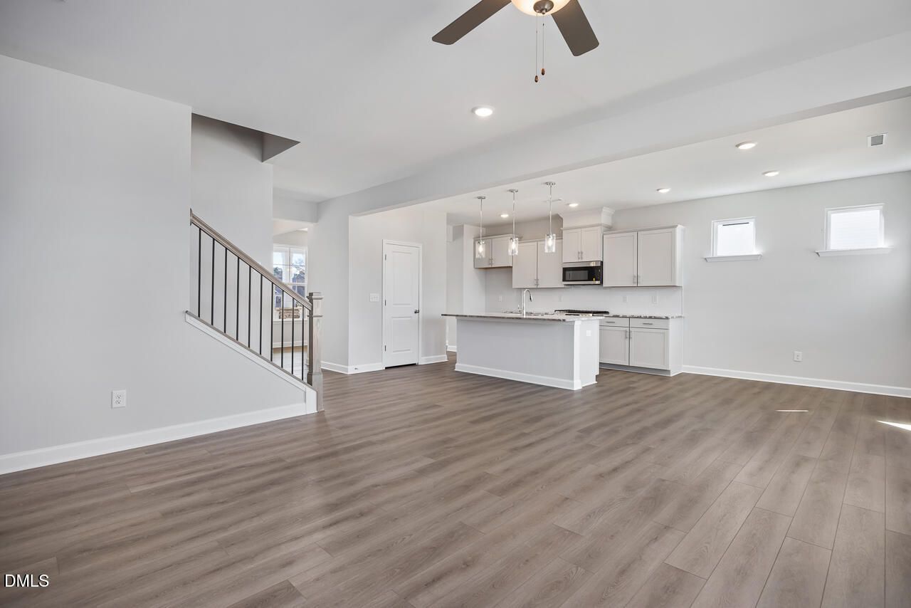 Open-concept kitchen with white cabinets, large island, hardwood floors, and staircase in Davidson Homes The Willow G, Angier NC