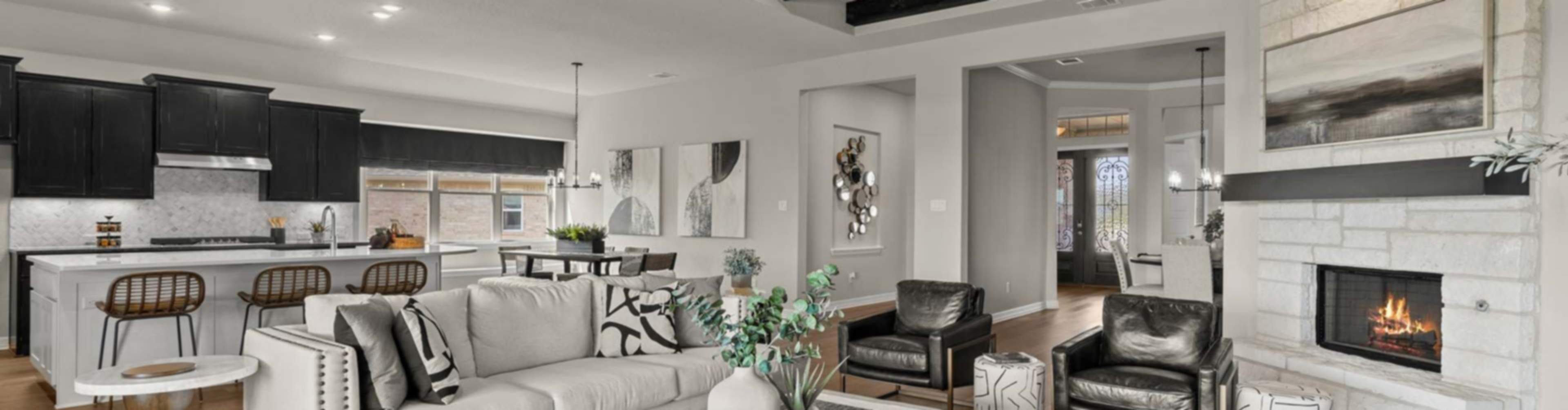 Spacious open-concept living room with white sofa, modern kitchen island, exposed beams, and fireplace in new Castroville home