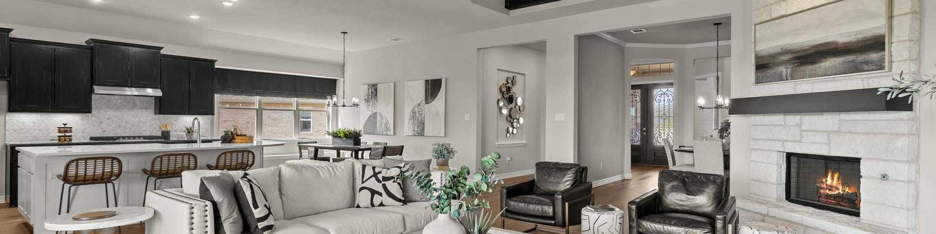 Spacious open-concept living room with white sofa, modern kitchen island, exposed beams, and fireplace in new Castroville home