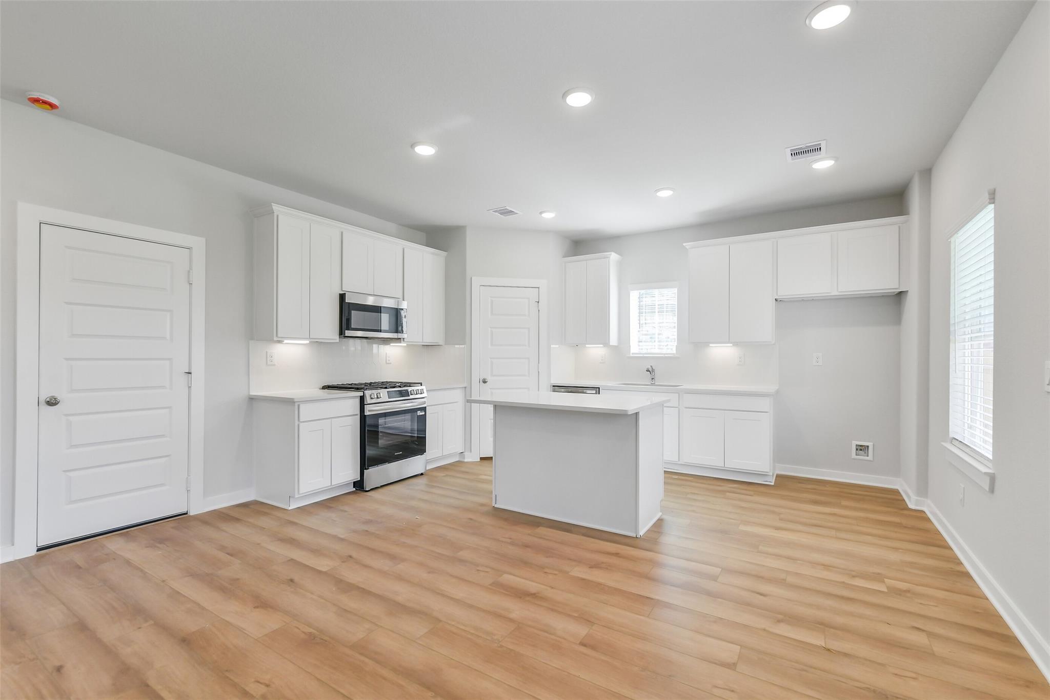 Modern white kitchen with central island, stainless steel oven and microwave in Davidson Homes The Trinity F, Magnolia, Texas