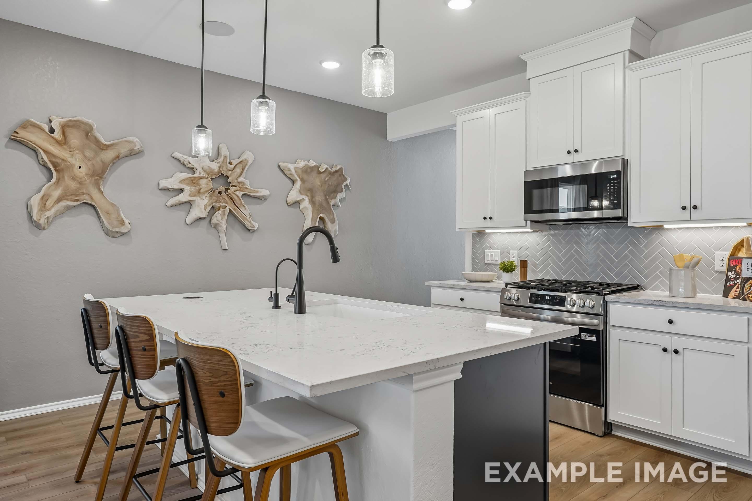 Modern kitchen in The Pinecrest featuring a large quartz island, white cabinetry, and a stylish herringbone backsplash.