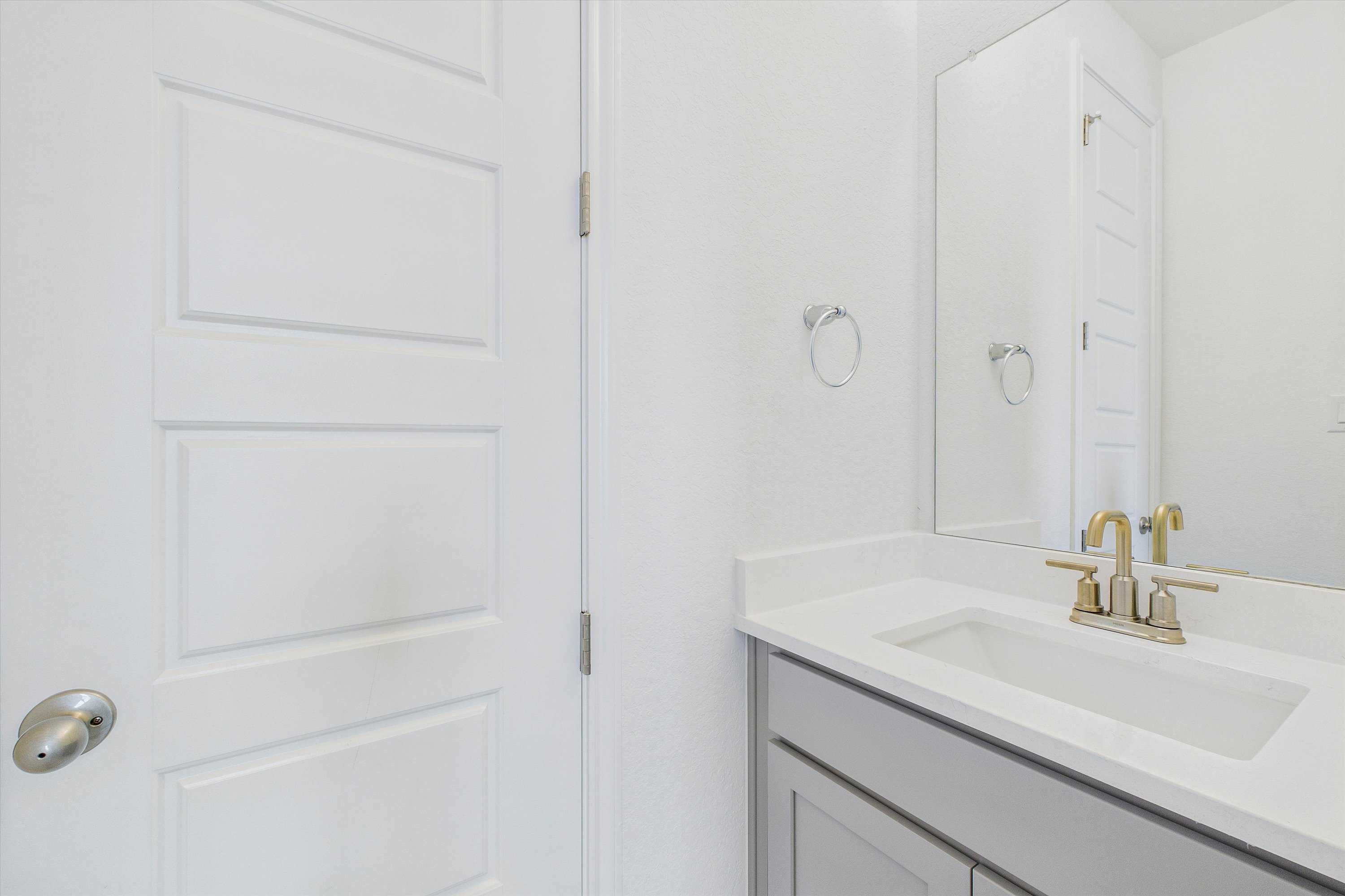 Elegant bathroom with white quartz vanity, gold faucet, frameless mirror in Davidson Homes Summerlin C, Castroville Texas