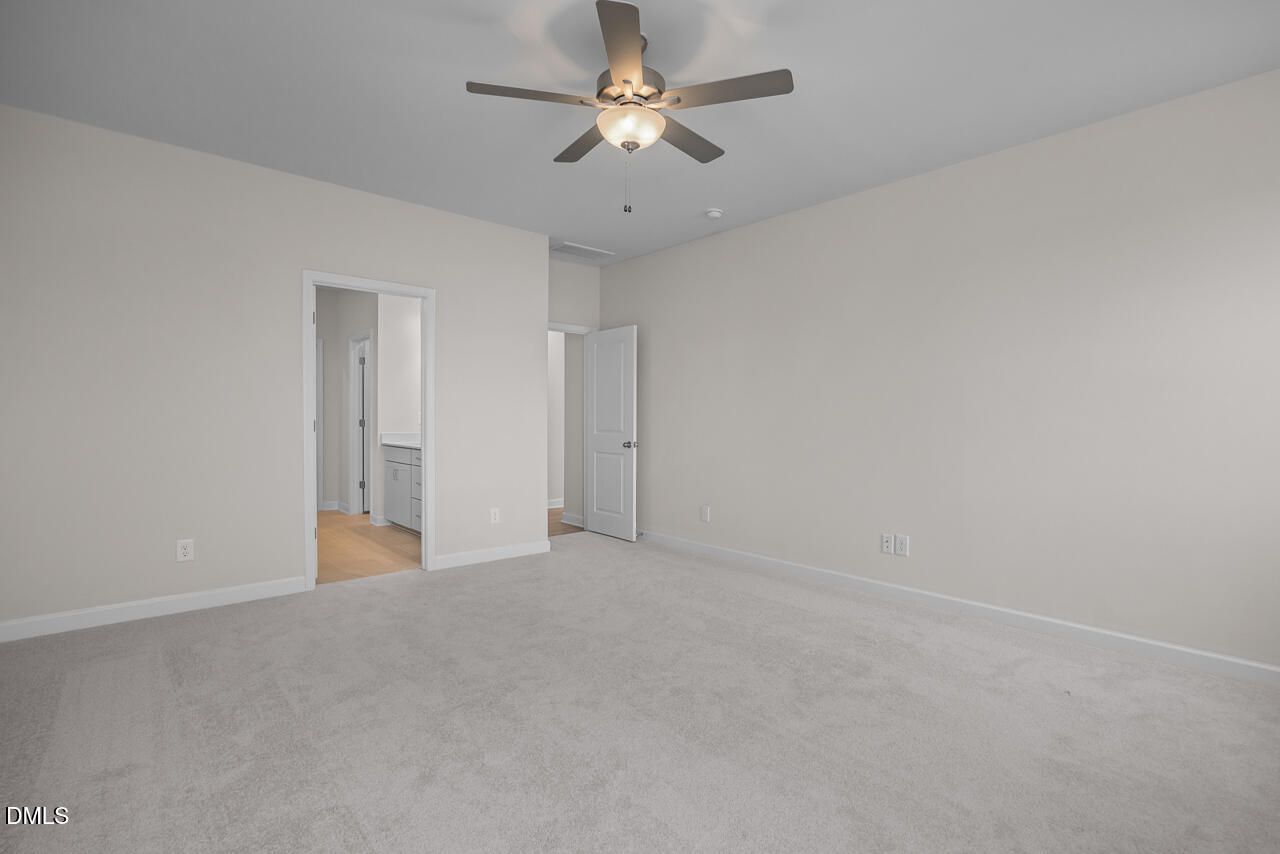Spacious bedroom with ceiling fan, beige walls, carpet floor, and en-suite bath in Davidson Homes The Cypress D II, Angier, NC