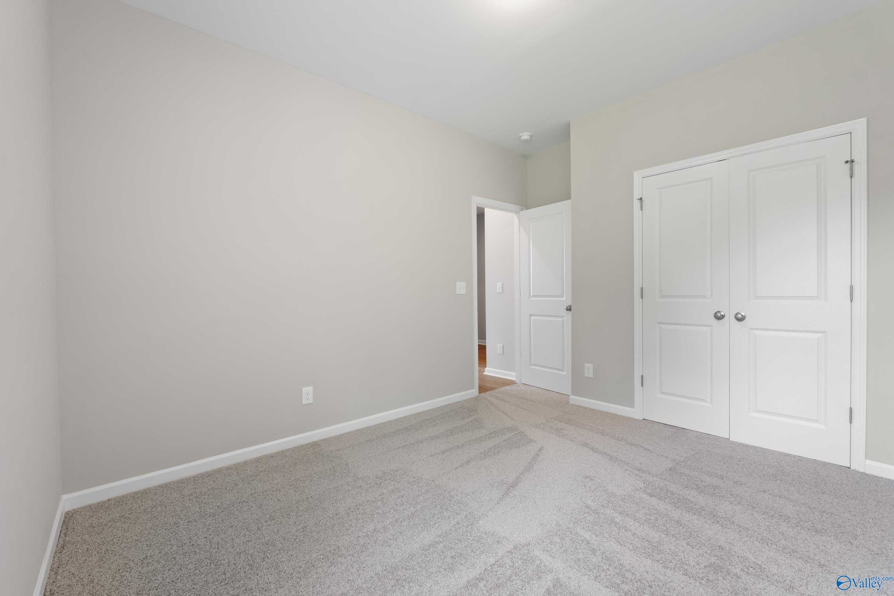 Spacious carpeted secondary bedroom with neutral gray walls, double closet doors, and bath access in Davidson Homes The Luna, Hazel Green, AL