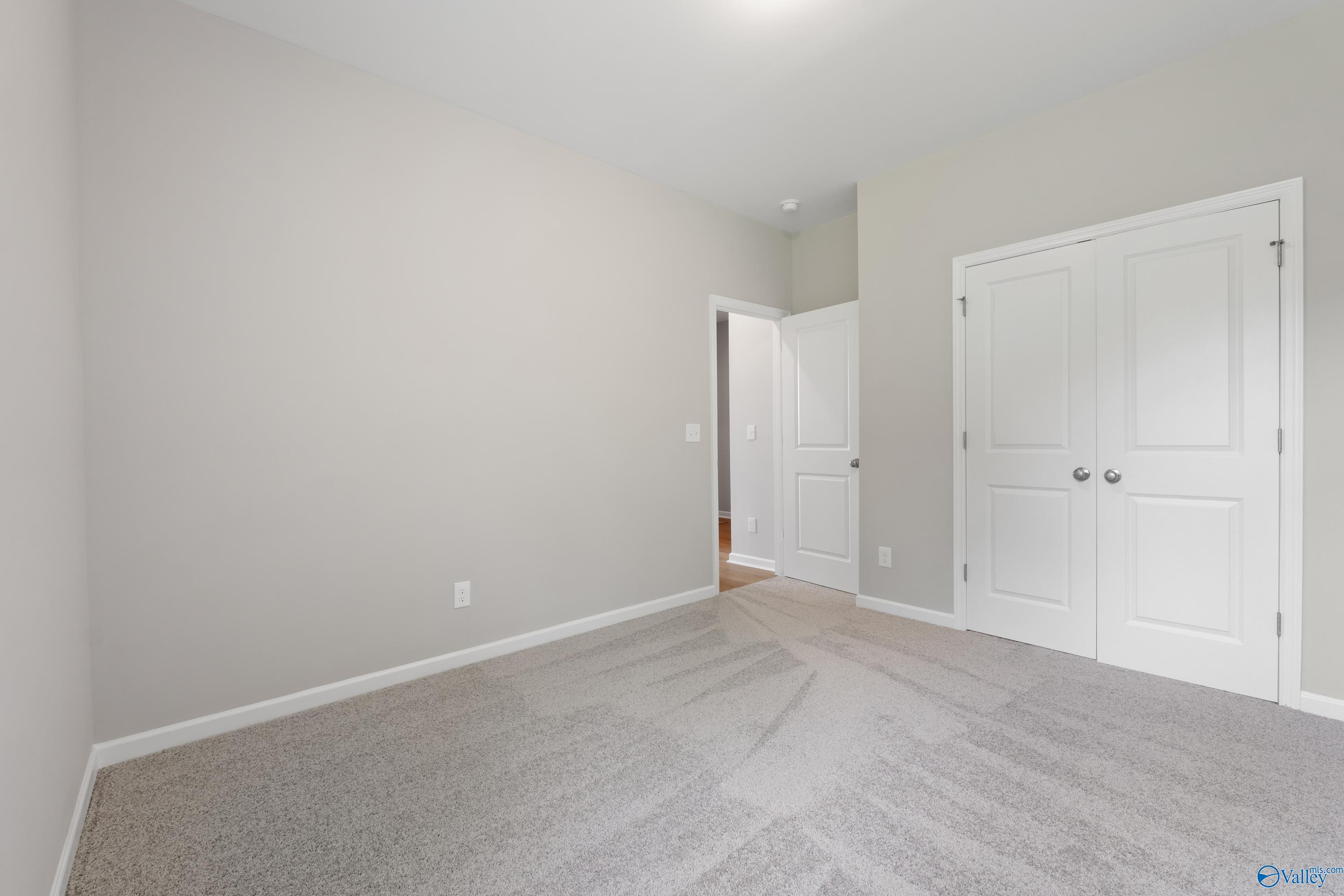 Carpeted bedroom with light gray walls, double-door closet, and open bathroom entry in Davidson Homes The Luna, Hazel Green, AL