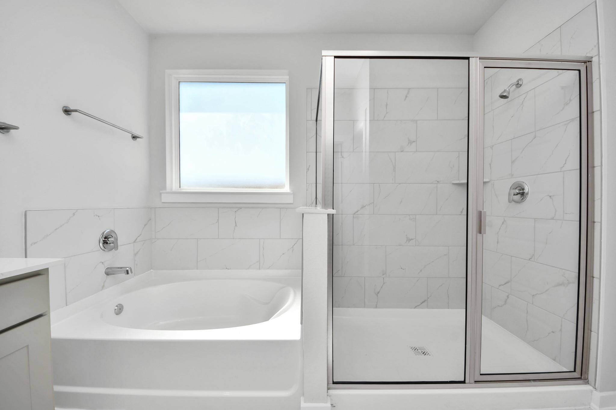 Modern primary bathroom with garden tub and glass-enclosed shower in The Riviera A floor plan at Emberly, Beasley, Texas.