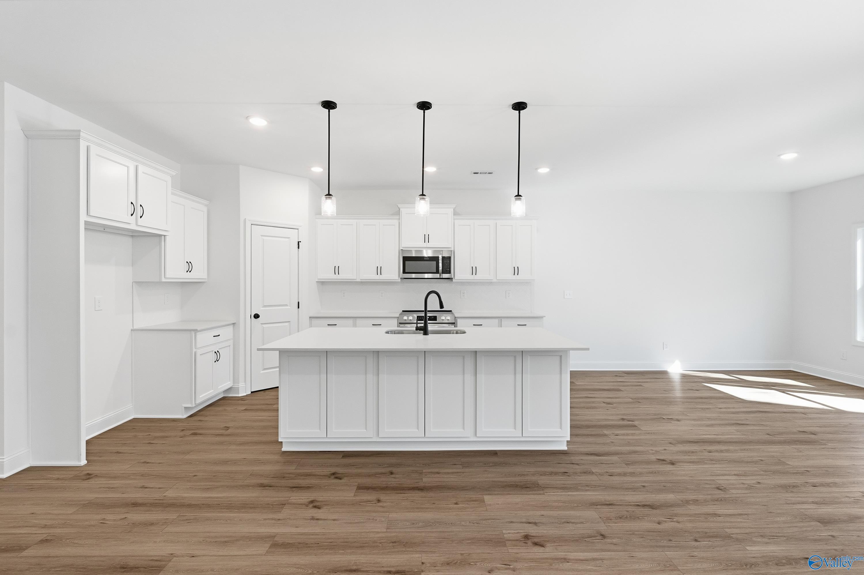 Modern white kitchen with oversized island, farmhouse sink, pendant lights, and hardwood floors in Davidson Homes Rockford D, Hazel Green AL